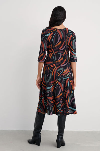 Woman wearing a patterned midi dress with black boots on a white background