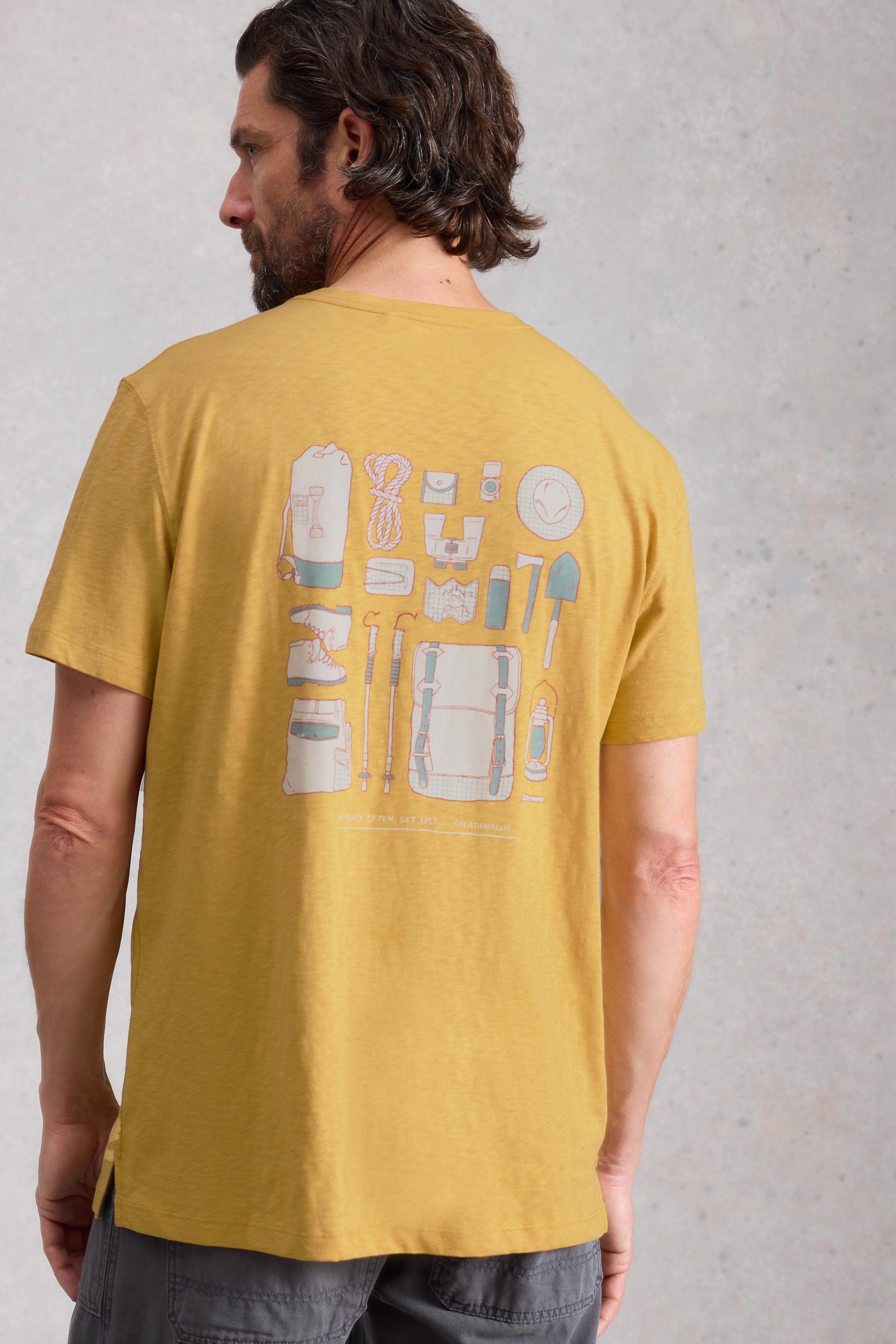 Man wearing a mustard yellow cotton t-shirt with graphic design on the back against a gray background