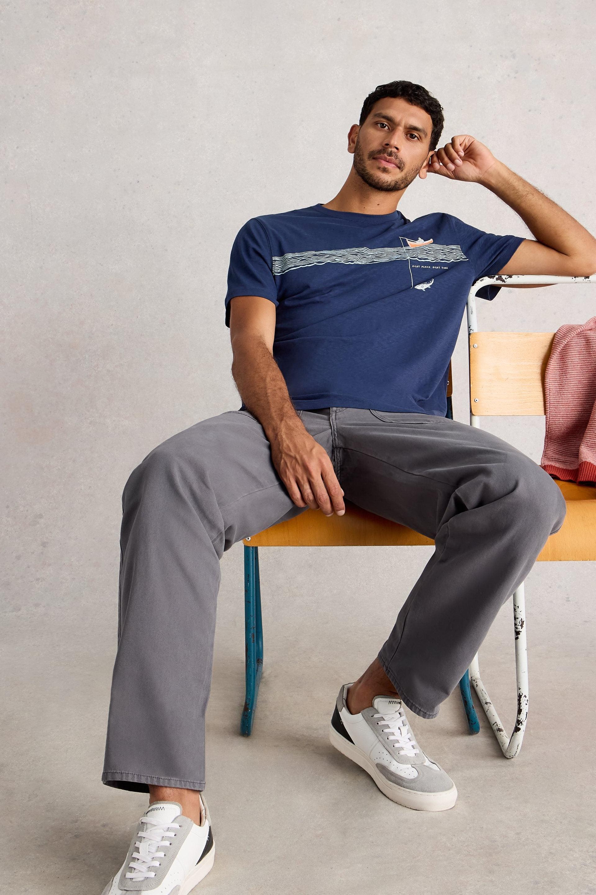 Man sitting on a chair wearing a blue cotton t-shirt and gray pants.