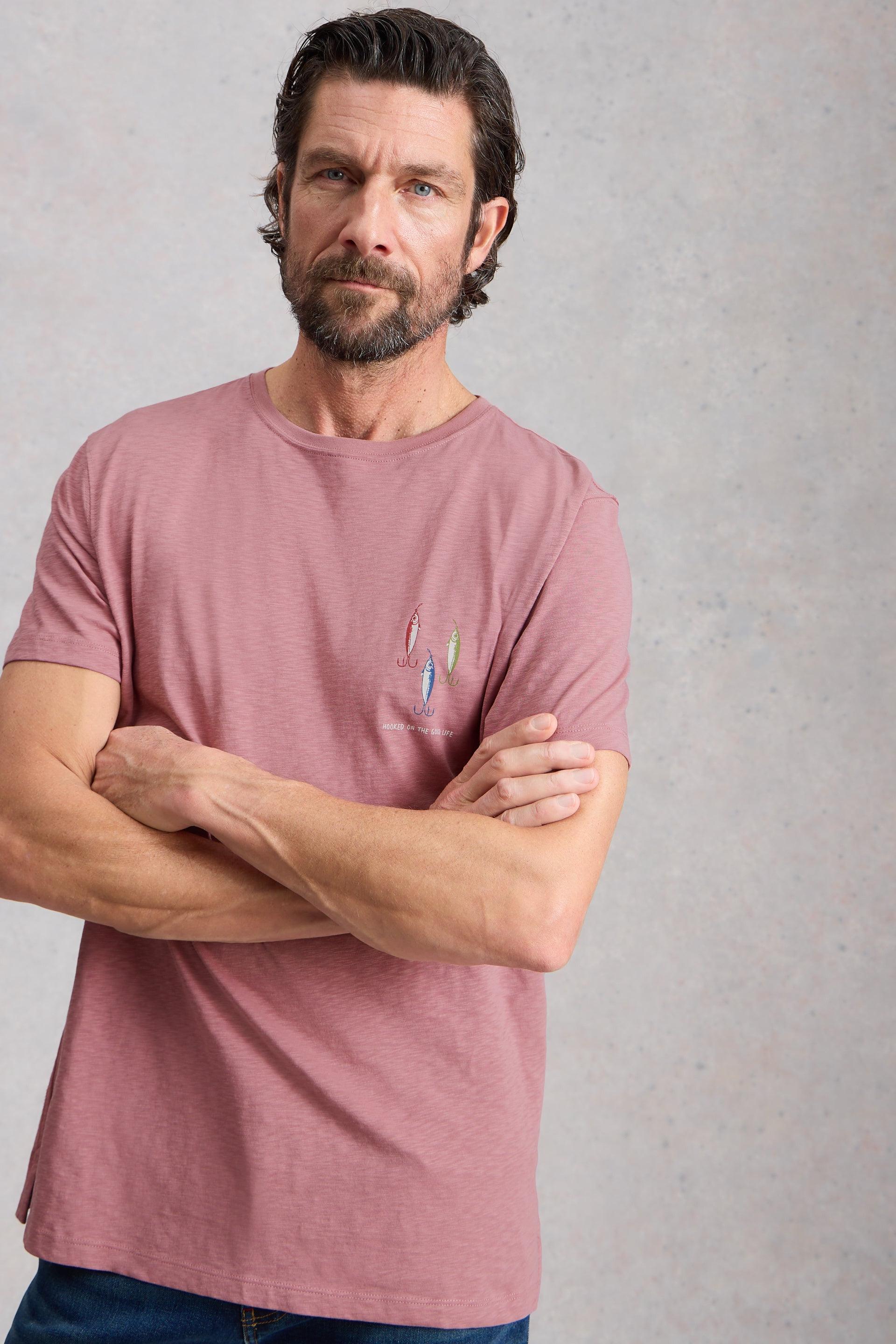 Man wearing a pink cotton t-shirt with a small logo on a gray background