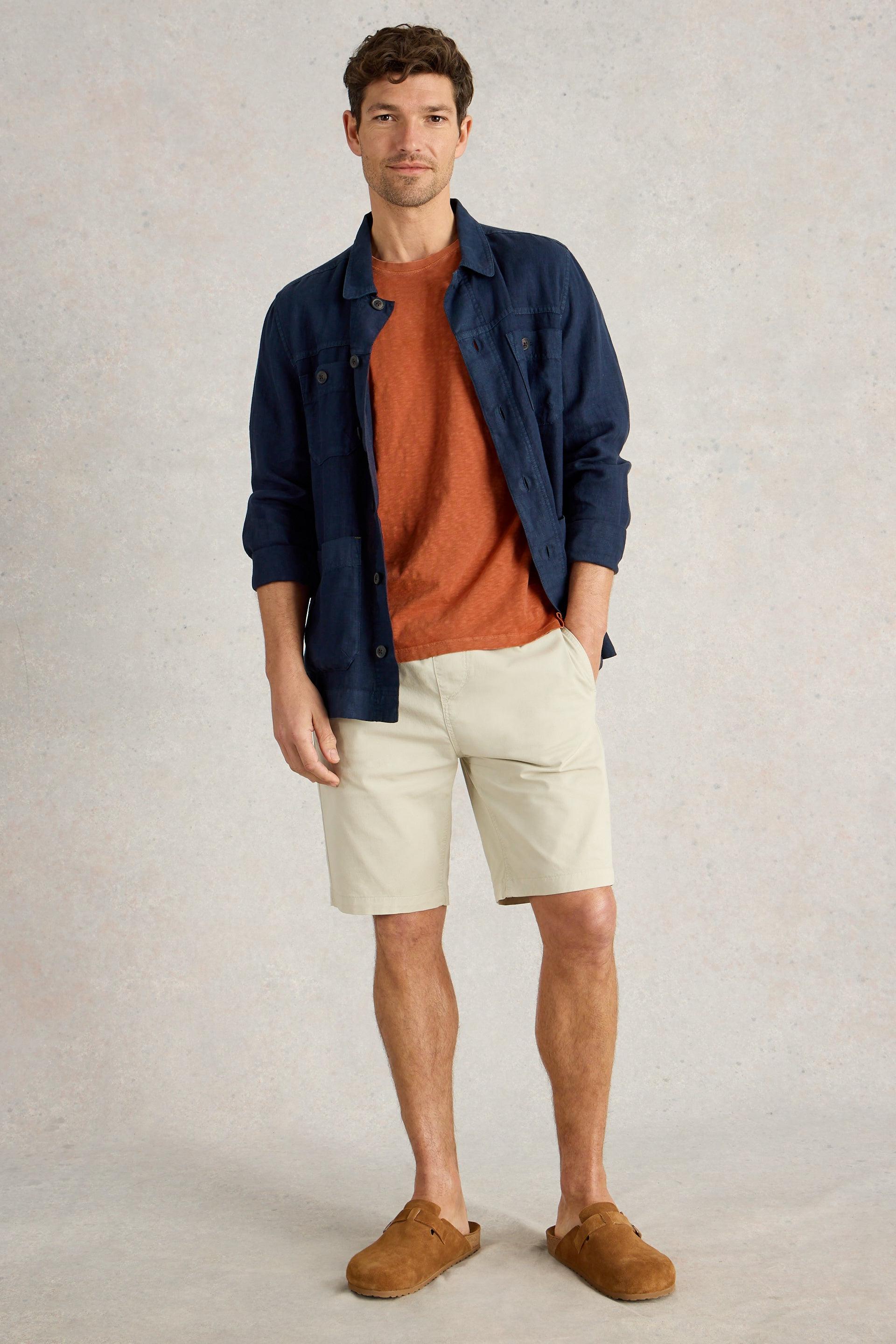 Model wearing orange t-shirt with a navy shirt, cream shorts and brown clogs.