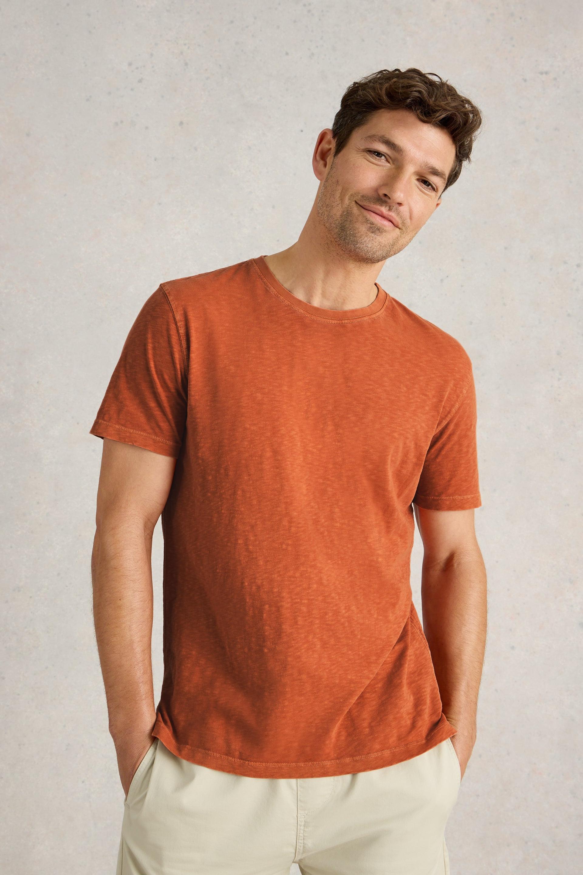 Model with hands in pockets wearing orange cotton sleeveless t-shirt.