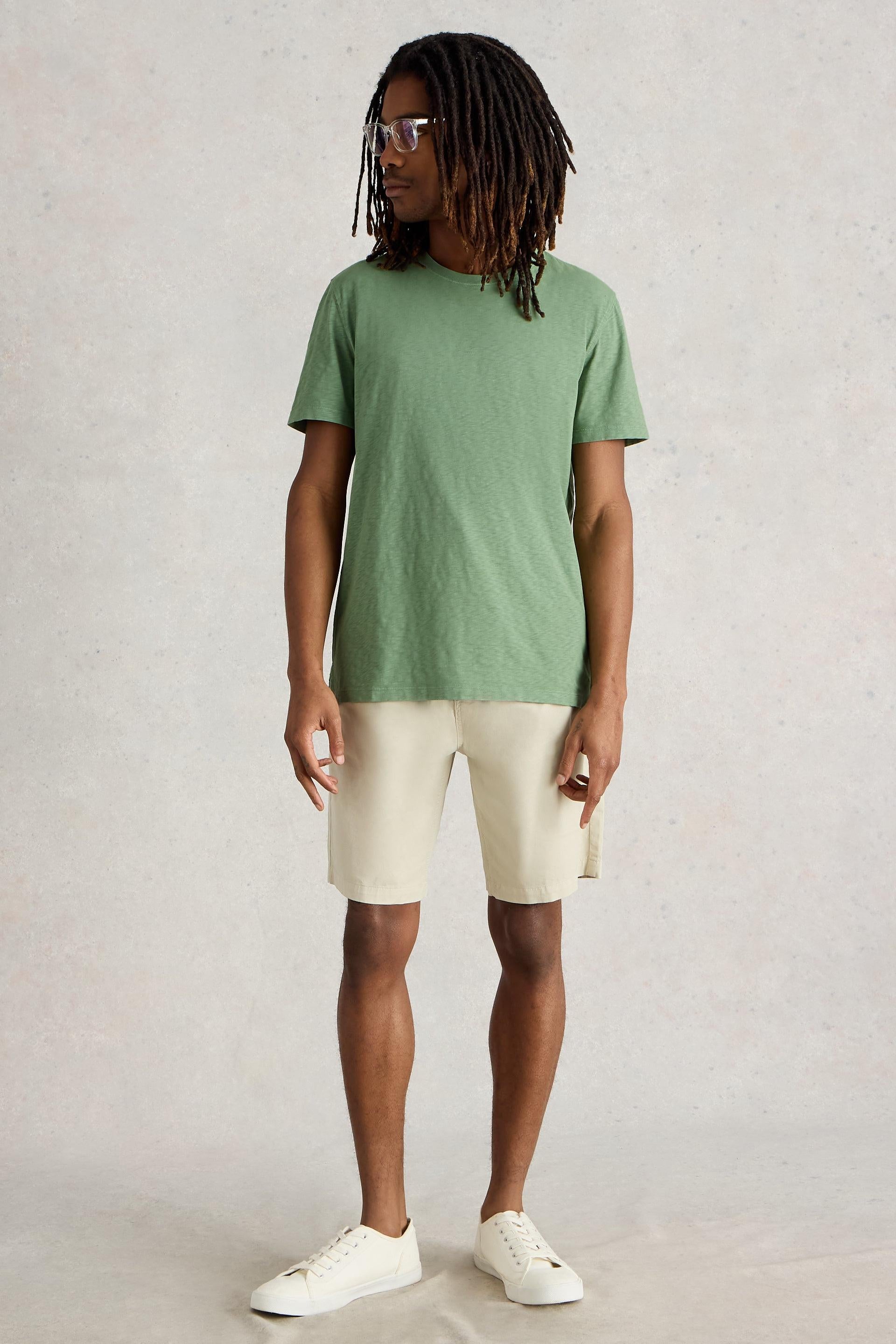 Model wearing green cotton t-shirt paired with ecru shorts and white trainers