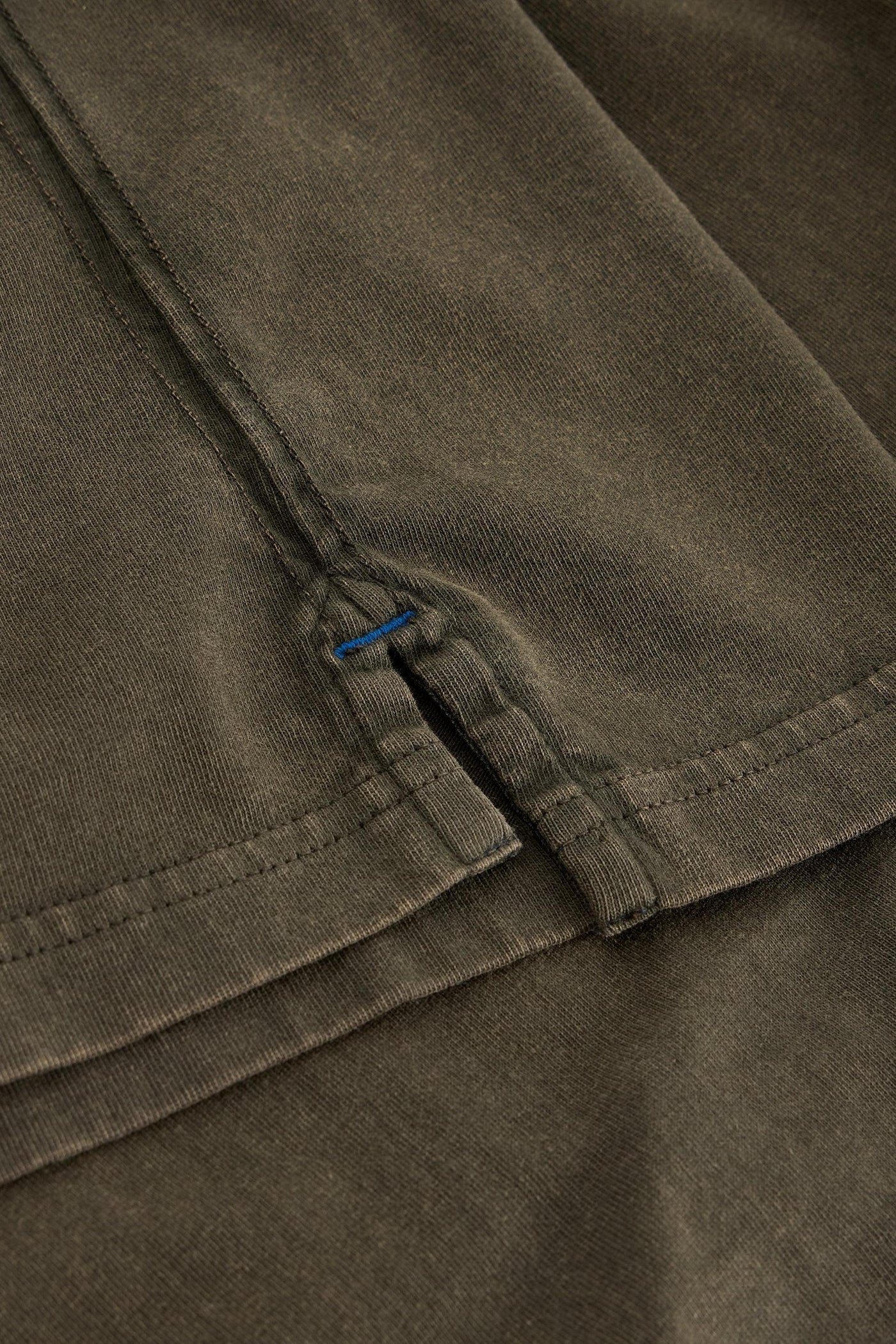 Close up of split length and blue stitching on long sleeve green organic cotton t-shirt