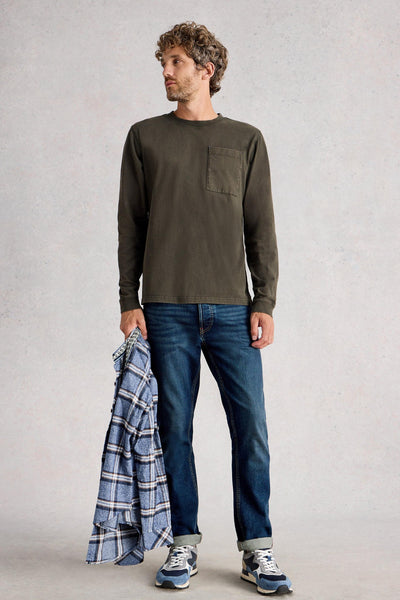 Man wearing long sleeve green organic cotton t-shirt, styled with blue denim jeans and blue sneakers, holding a blue shacket.