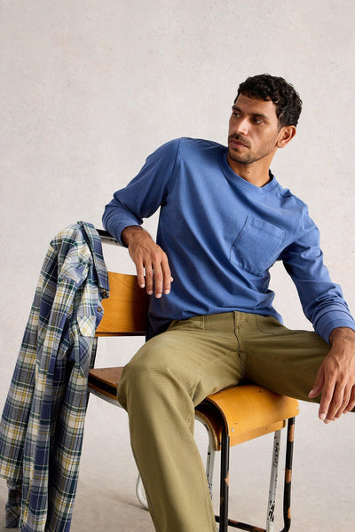 Man sitting in chair wearing long sleeve blue organic cotton t-shirt styled with khaki green trousers