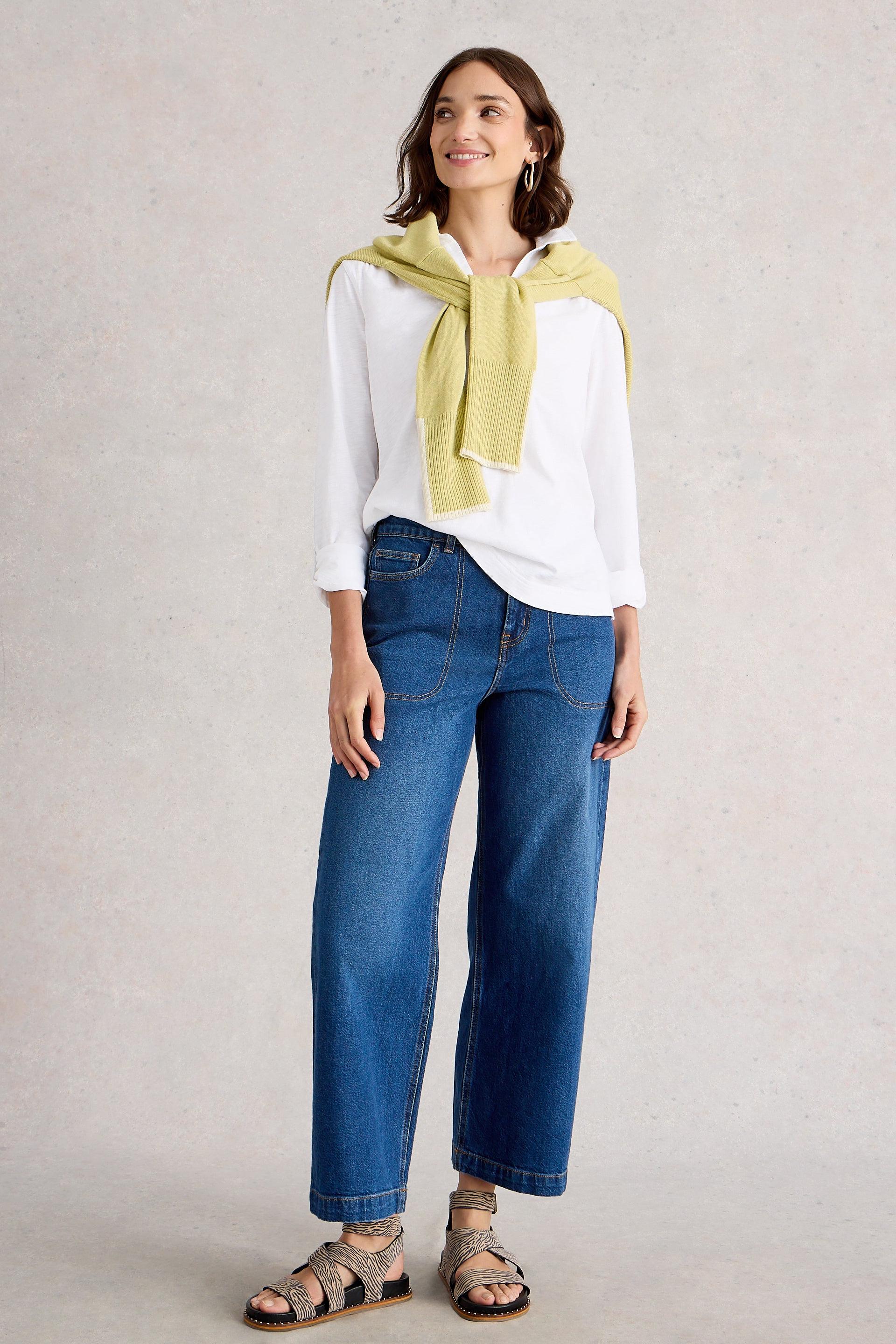 Woman wearing a white cotton blouse, blue jeans, and a yellow scarf against a plain background