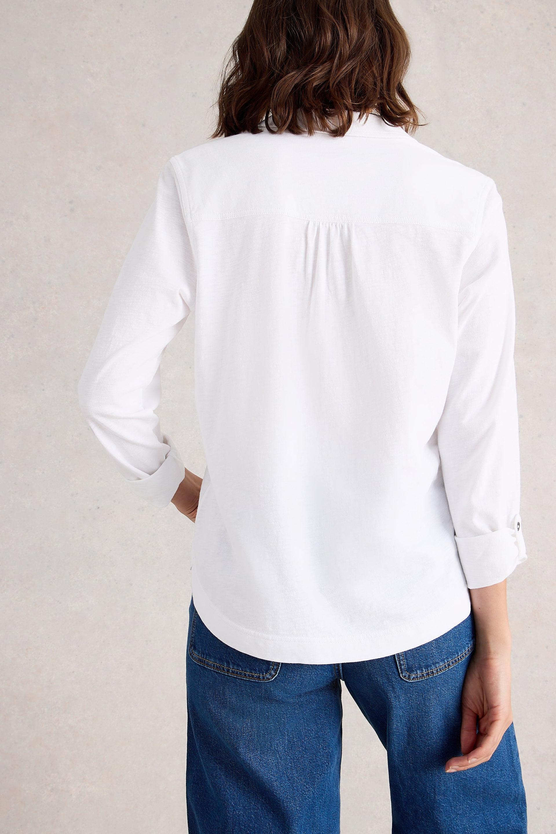 Person wearing a white cotton blouse and blue jeans against a plain background