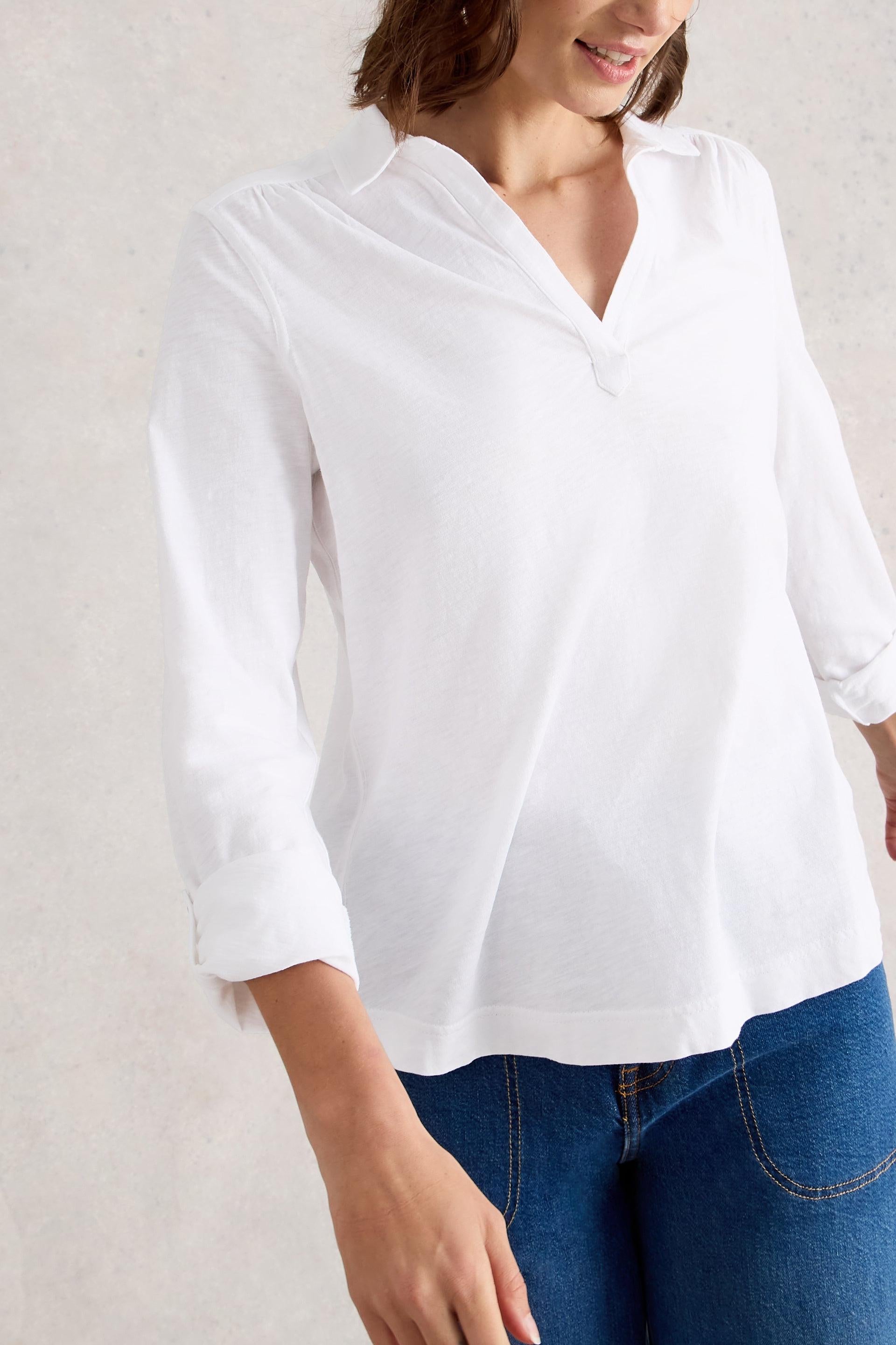 Person wearing a white cotton blouse and blue jeans against a light background