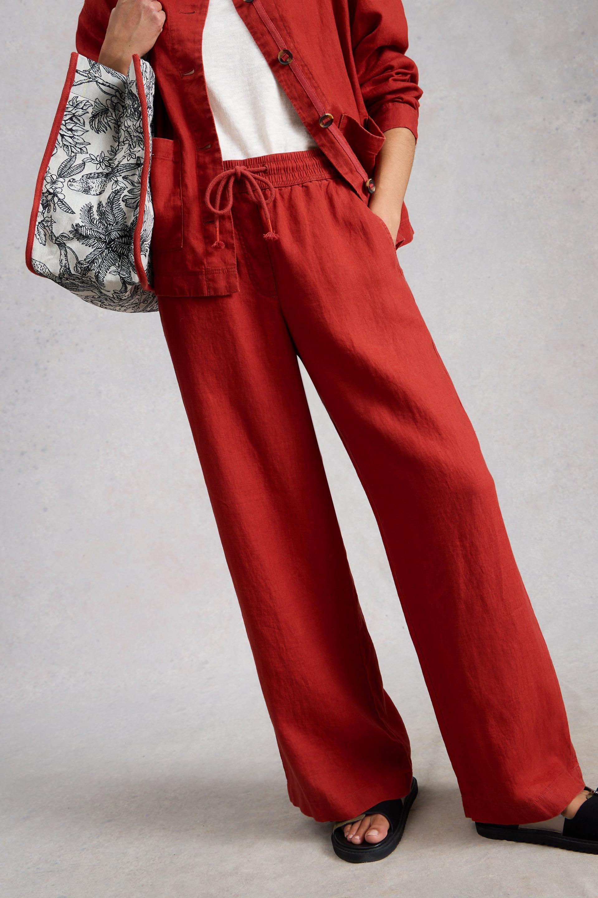 Person wearing a red outfit with wide-leg linen pants and a matching linen jacket, holding a patterned bag.