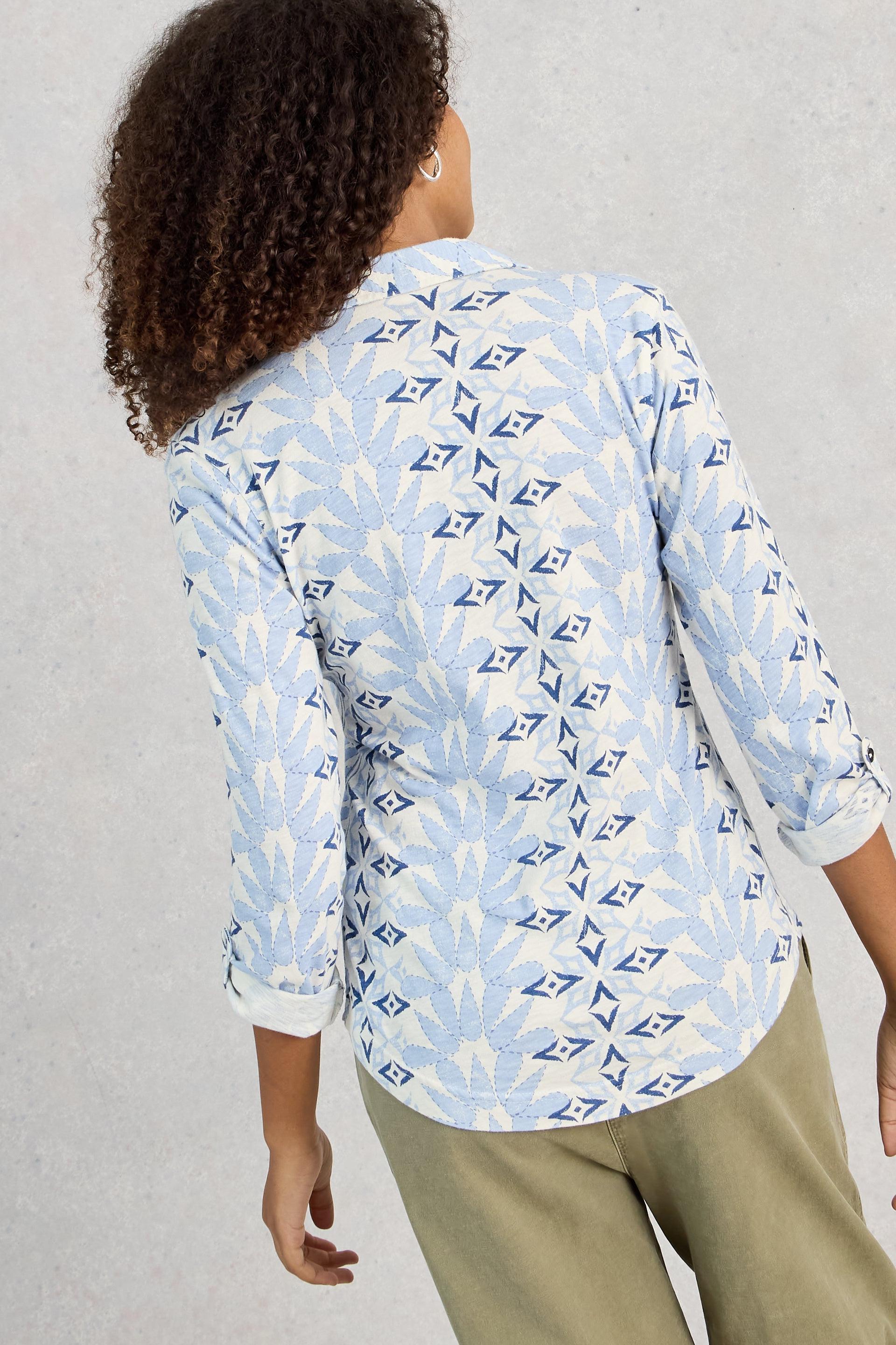 Person wearing a light blue patterned shirt with rolled-up sleeves on a gray background