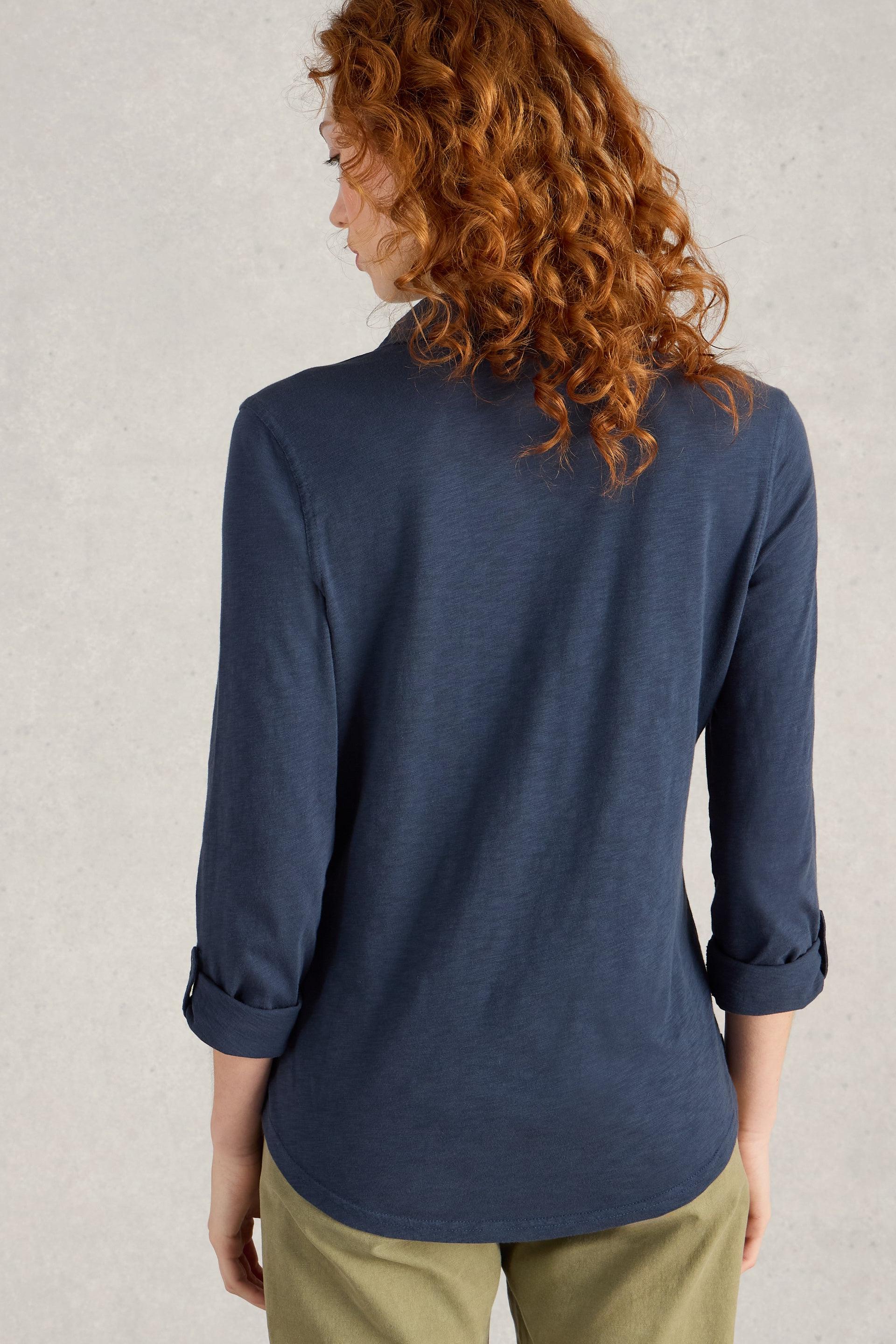 Person wearing a navy blue shirt with rolled-up sleeves on a light gray background