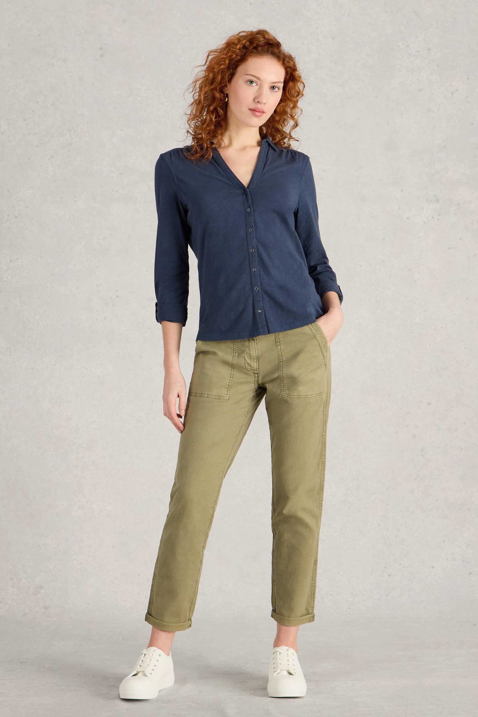 Woman wearing a blue cotton shirt and green pants against a plain background