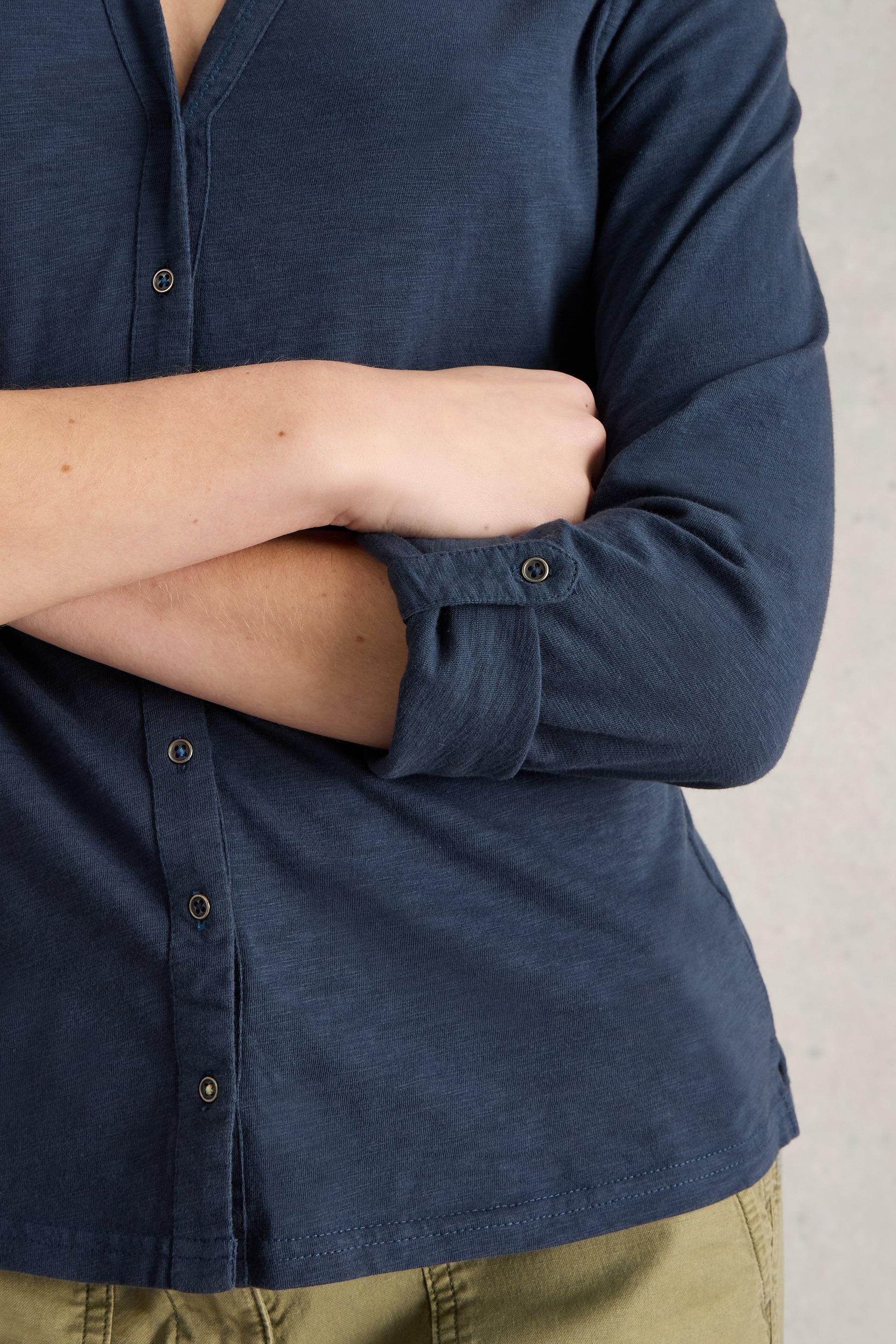 Person wearing a navy blue button-up shirt with rolled-up sleeves on a neutral background