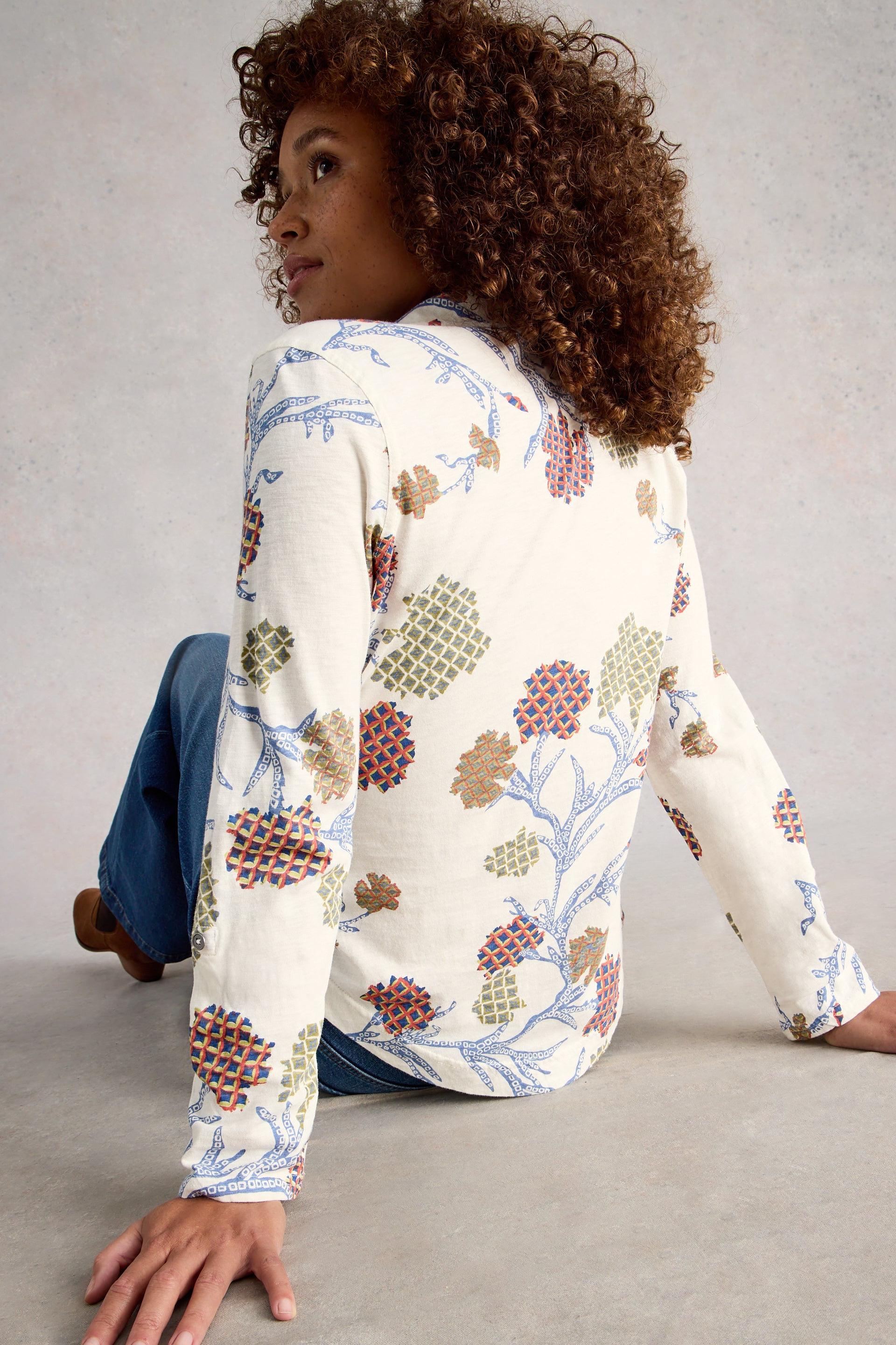 Woman wearing a floral patterned shirt sitting on the floor against a plain background