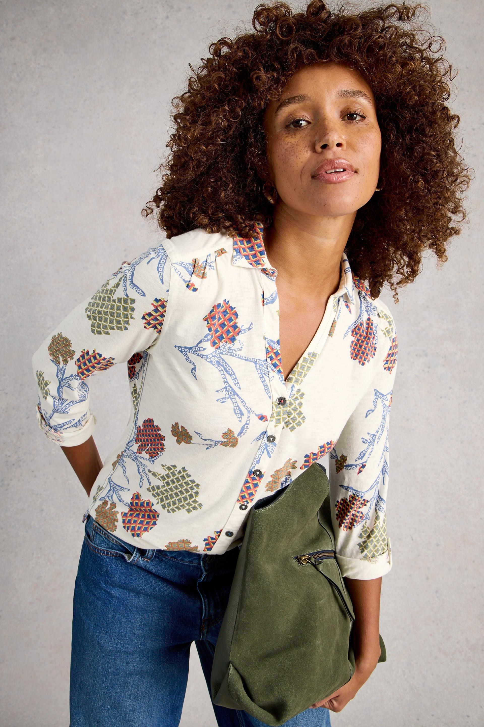 Woman wearing a patterned cotton blouse and holding a green bag against a gray background