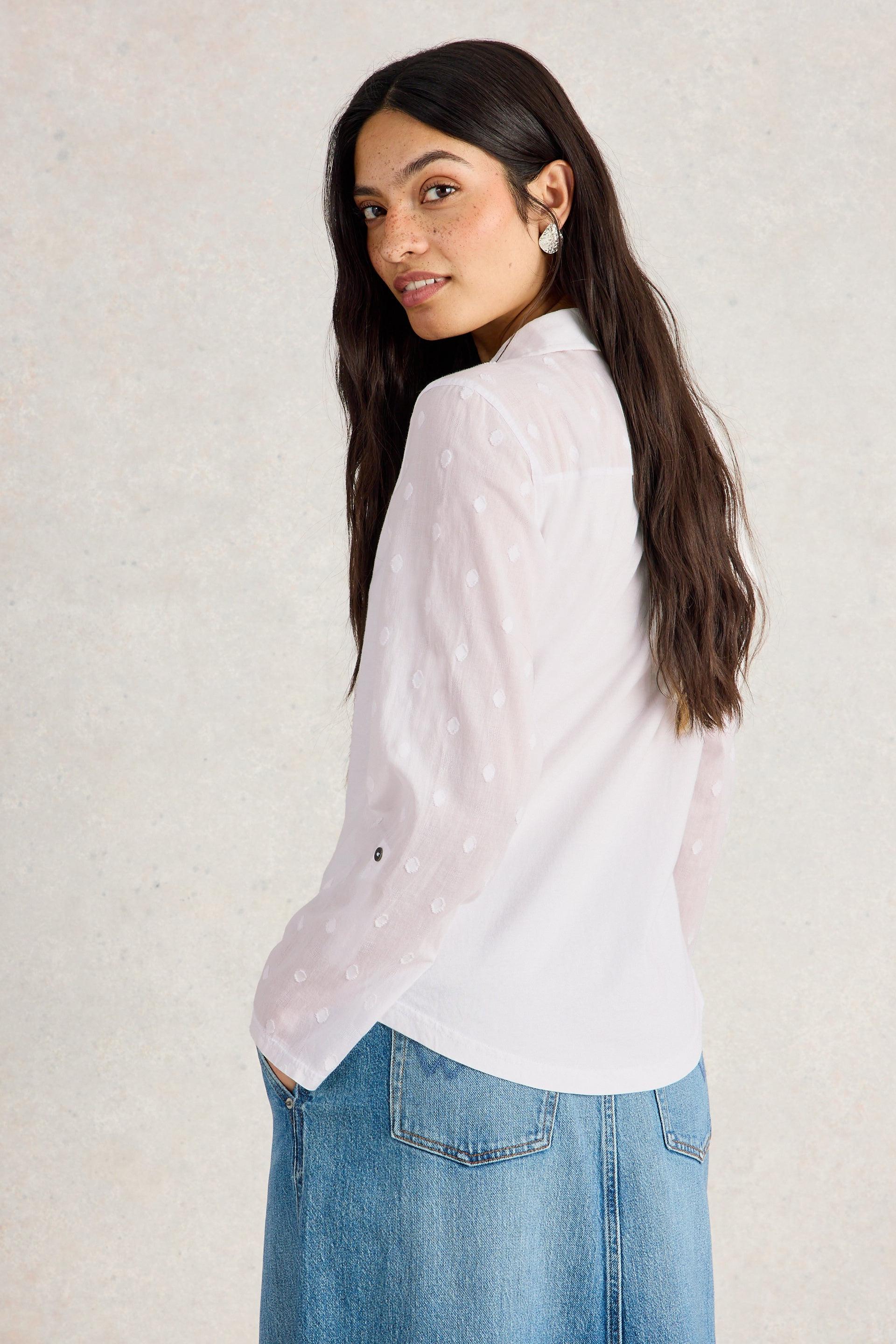 Woman wearing a white blouse and blue jeans against a plain background
