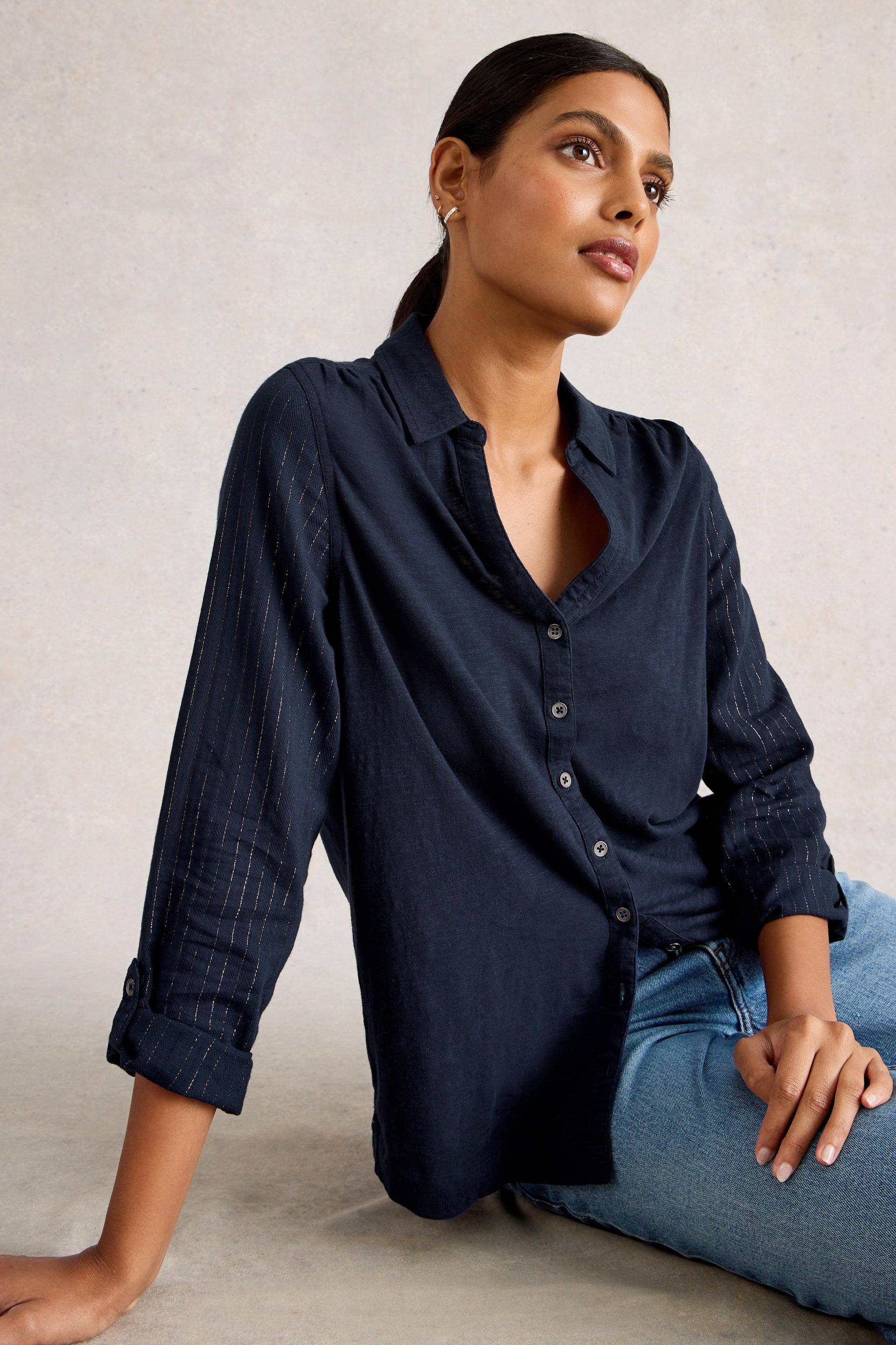 Woman wearing a navy blue button-up shirt and jeans against a neutral background