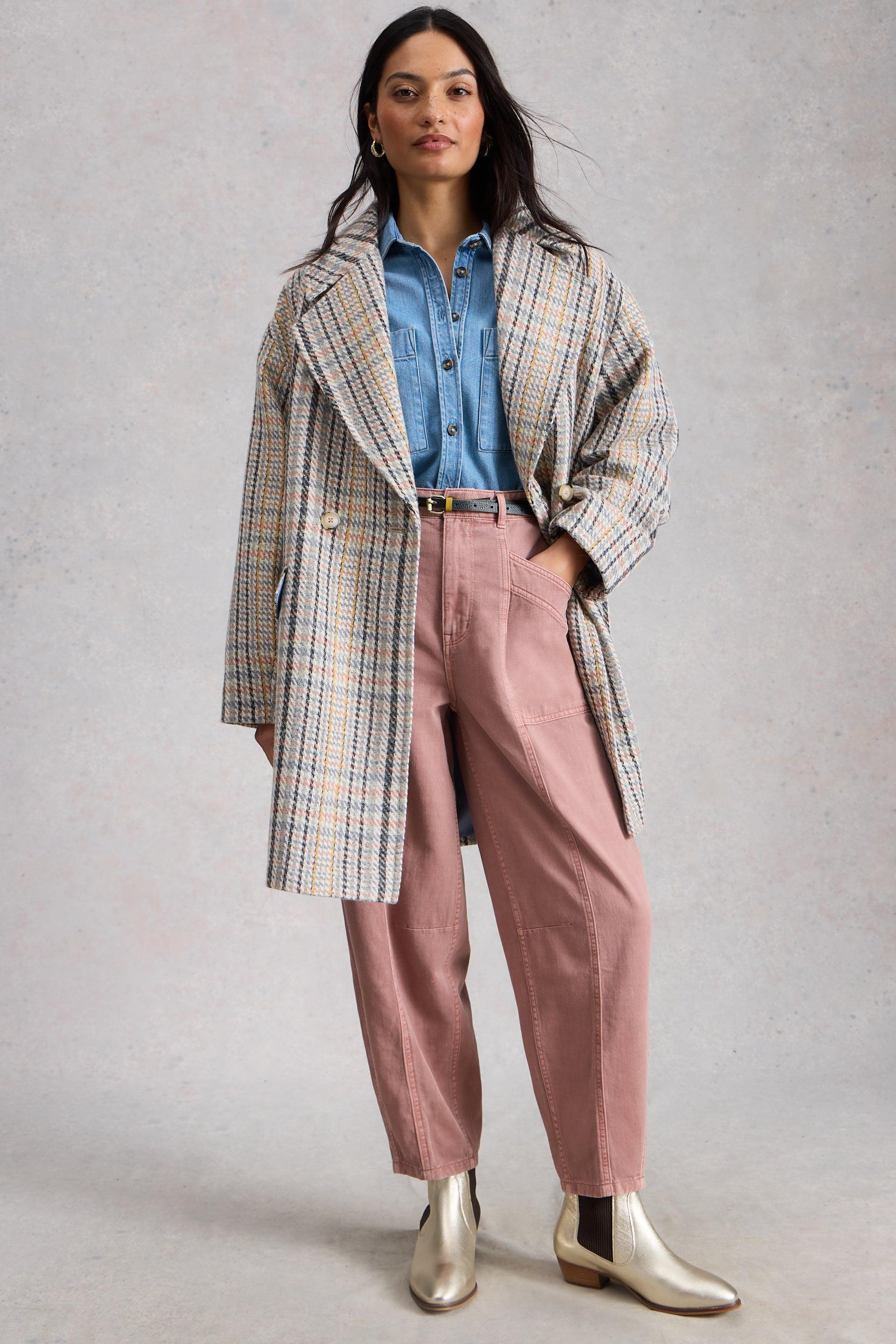 Woman wearing a plaid coat, blue shirt, pink cotton pants, and silver boots on a gray background