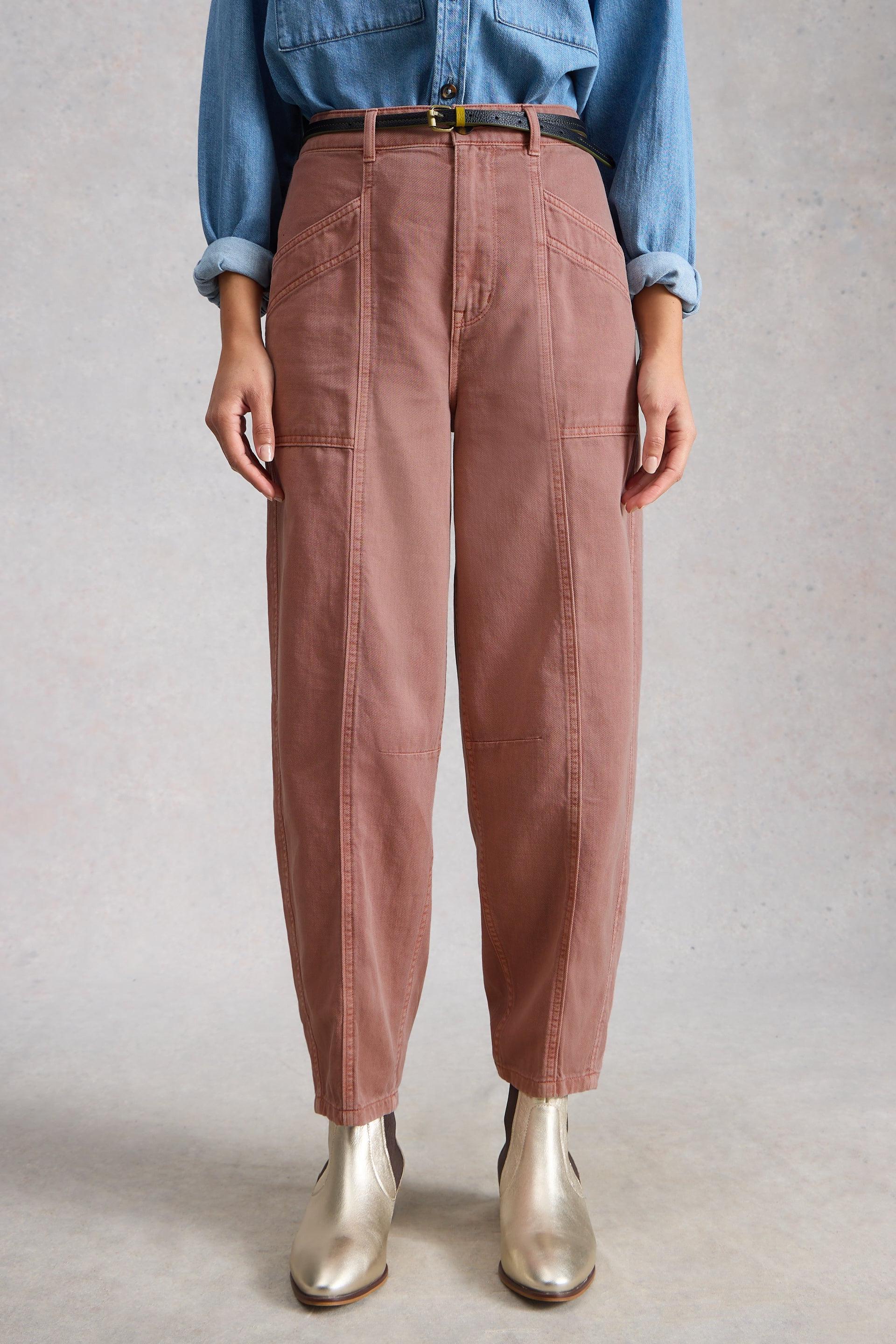 Person wearing pink organic cotton barrel trousers, blue shirt, and gold shoes against a neutral background