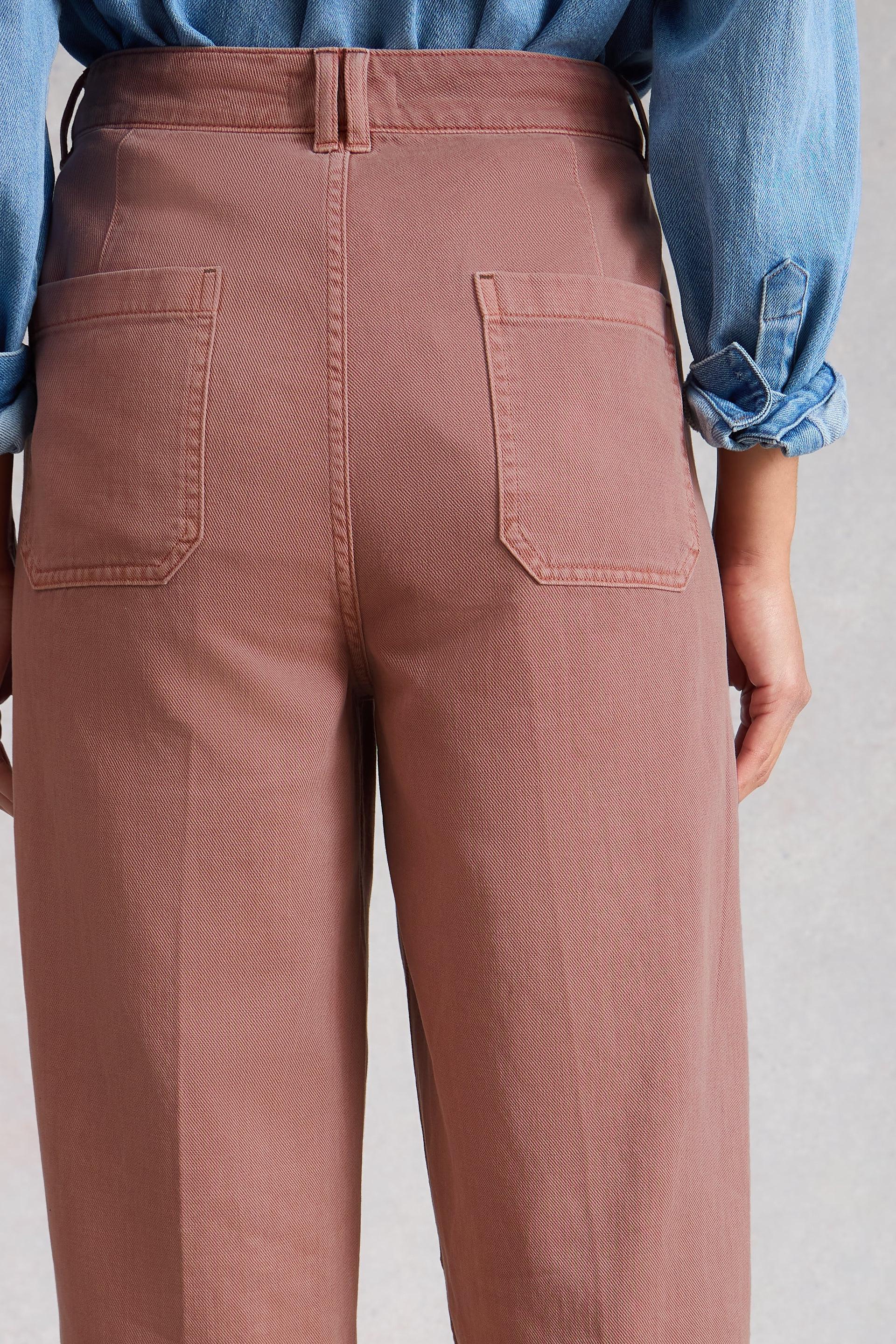 Person wearing pink barrel trousers with a blue shirt rolled up to the elbows on a plain background