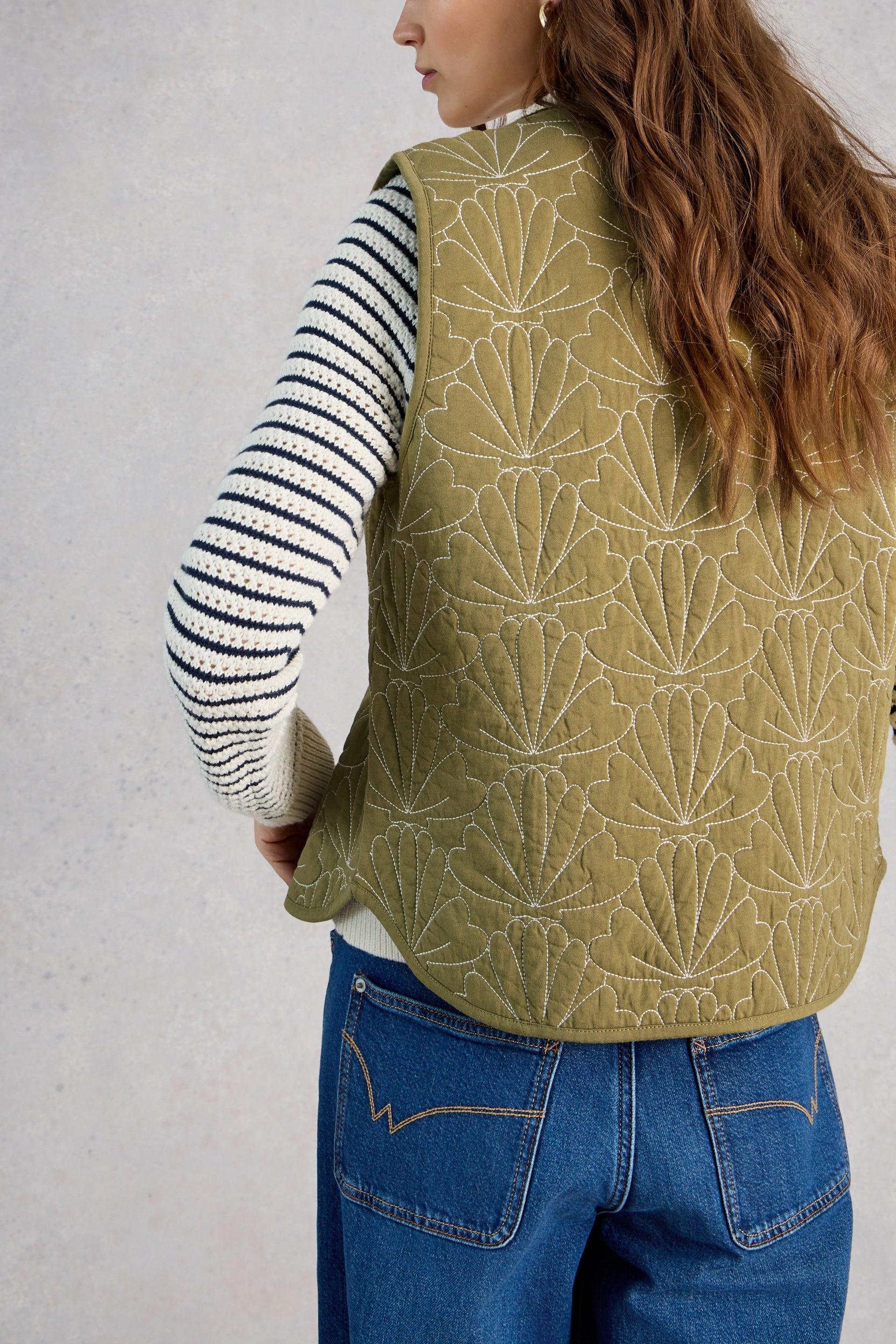 Model wearing a green quilted vest with a white and black striped shirt underneath, on a plain background.