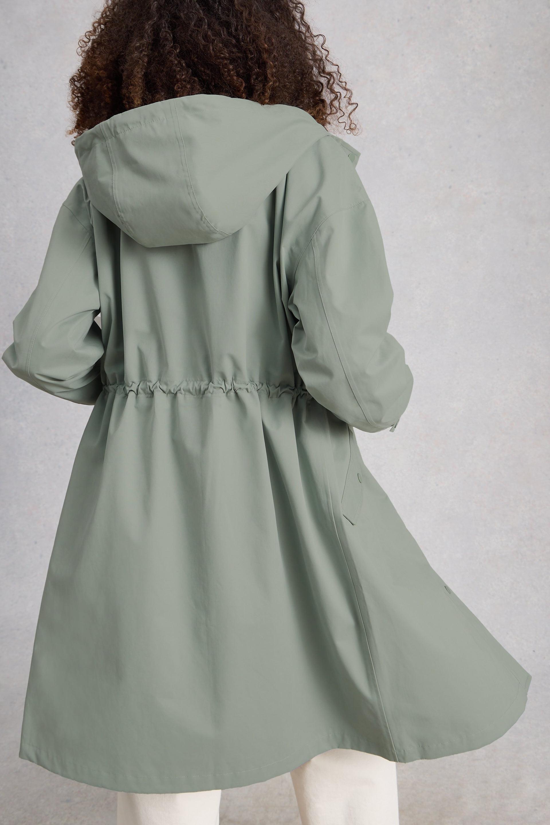 Person wearing a green waterproof raincoat on a plain background