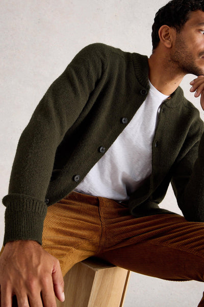 Man sitting on wooden box wearing woolen bomber cardigan with white t-shirt and orange ribbed trousers