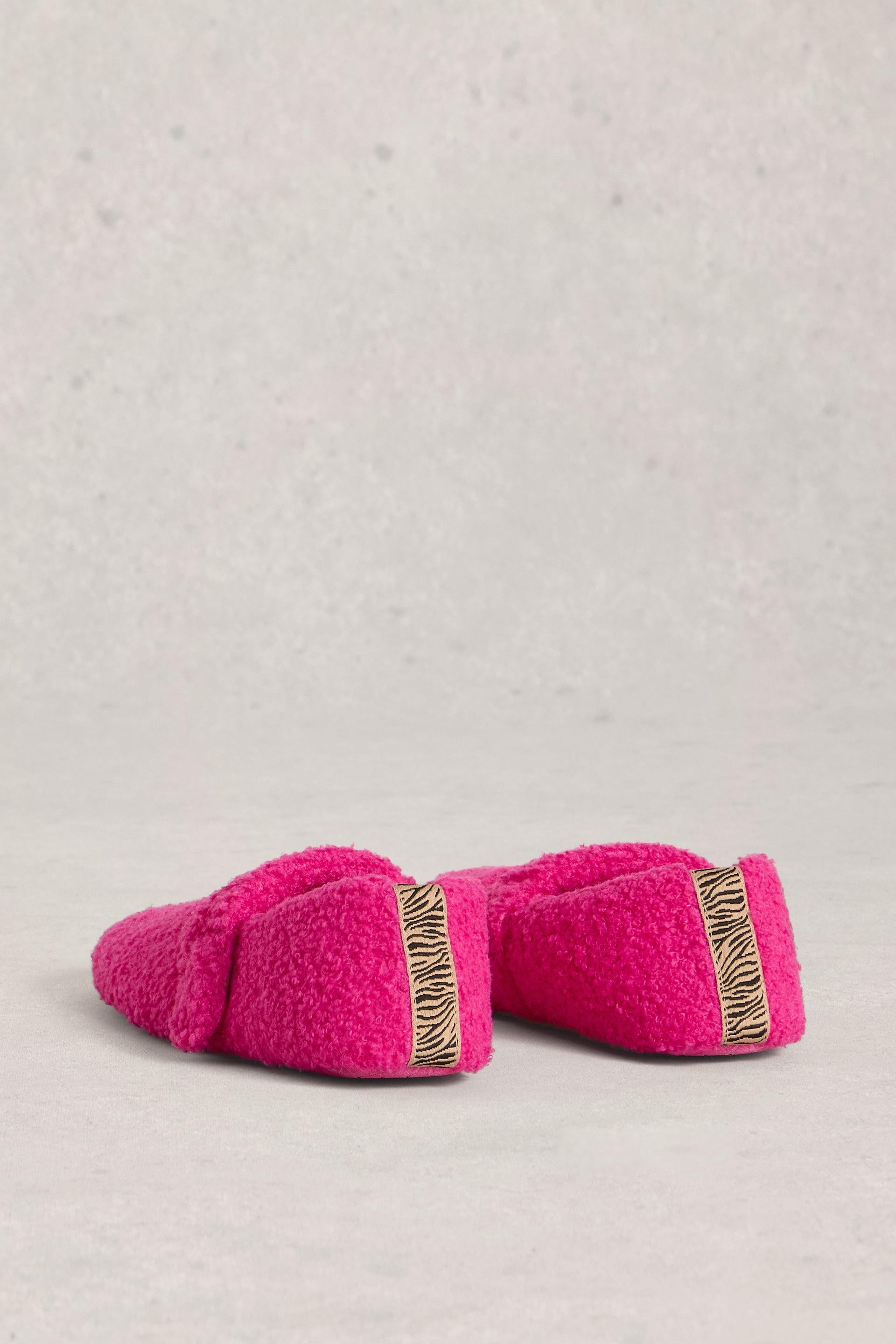 Pair of pink borg slippers with gold trim on a light gray background