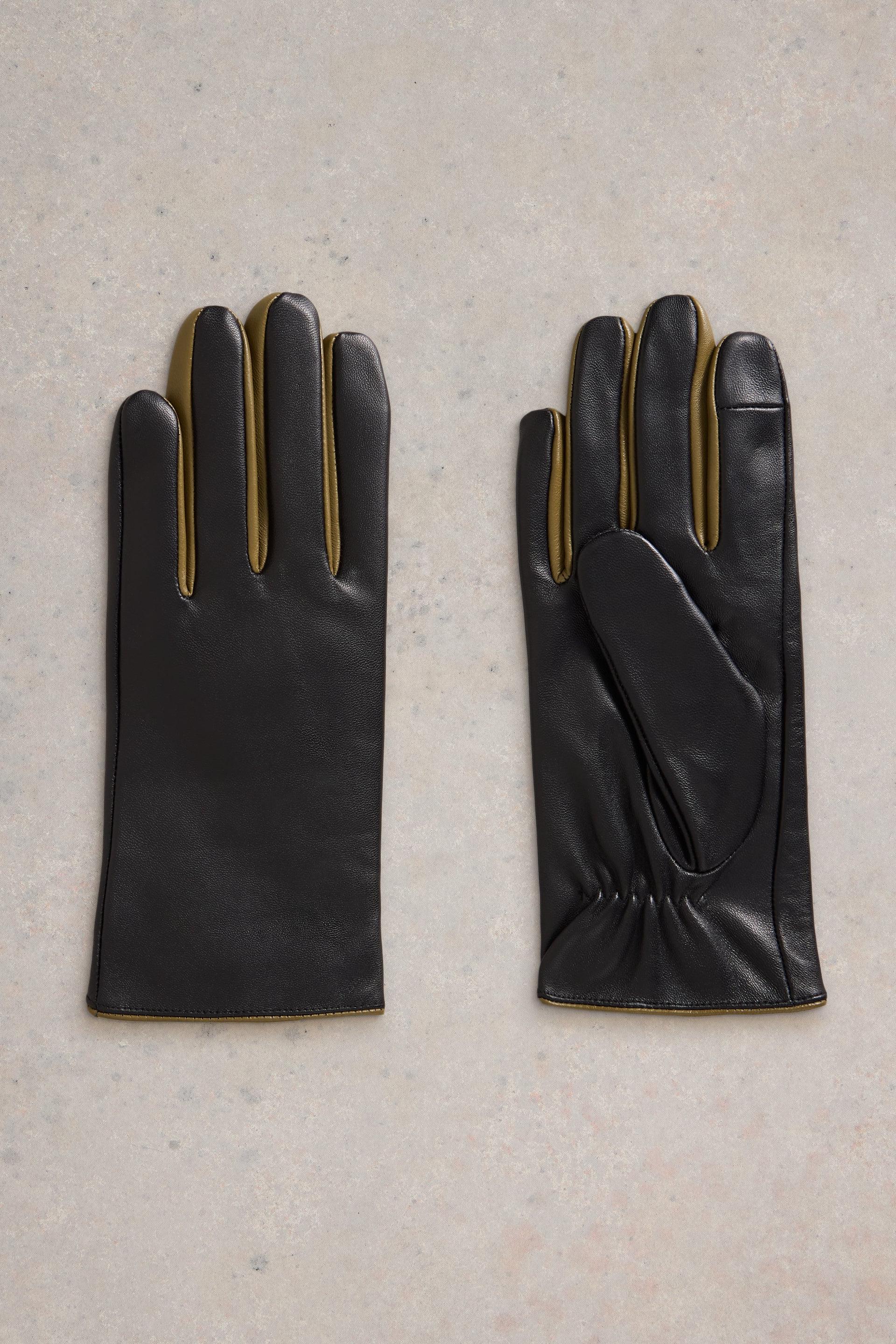 Flat lay of black leather gloves with mustard detail on a neutral background
