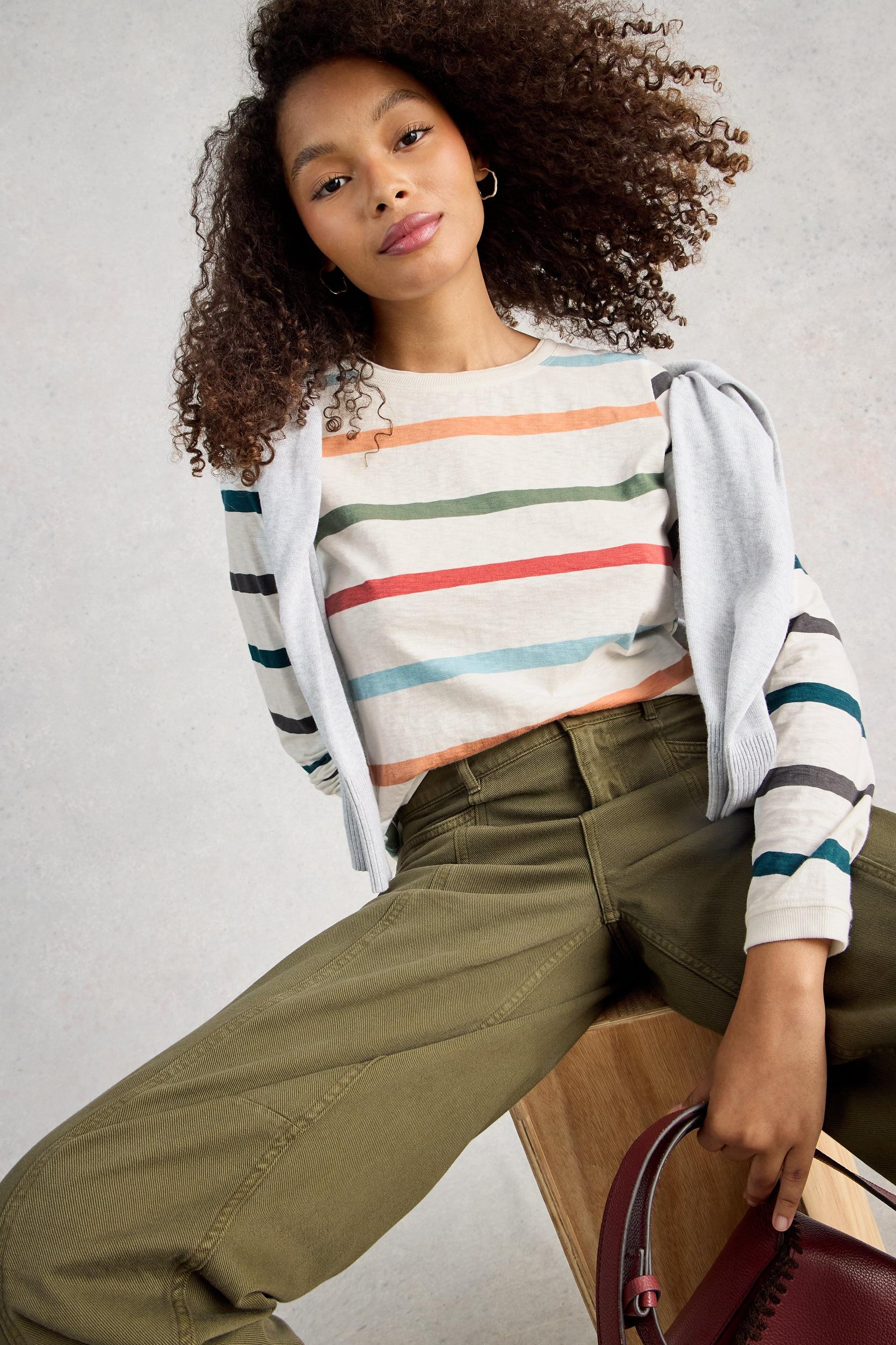 Model wearing a striped cotton t-shirt and green pants sitting on a wooden stool.
