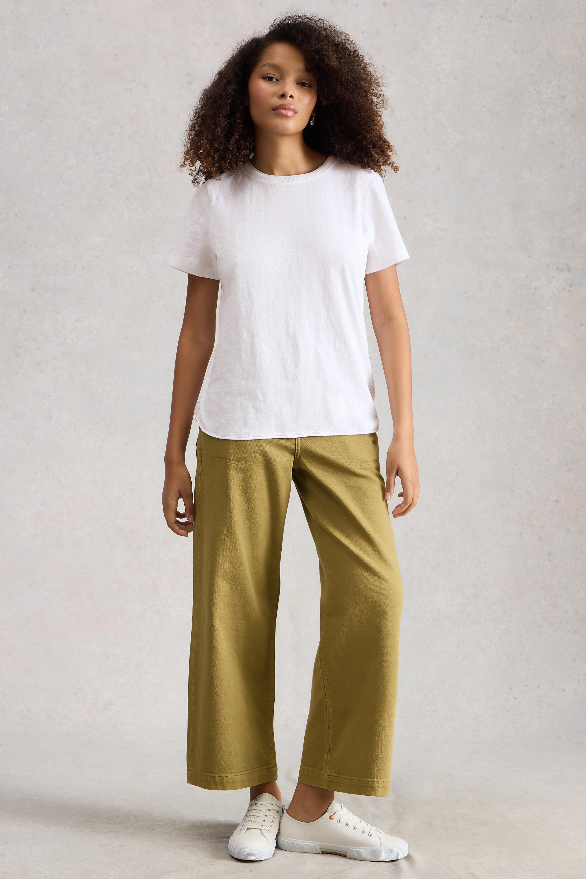 Woman wearing a white cotton t-shirt and mustard yellow pants on a plain background