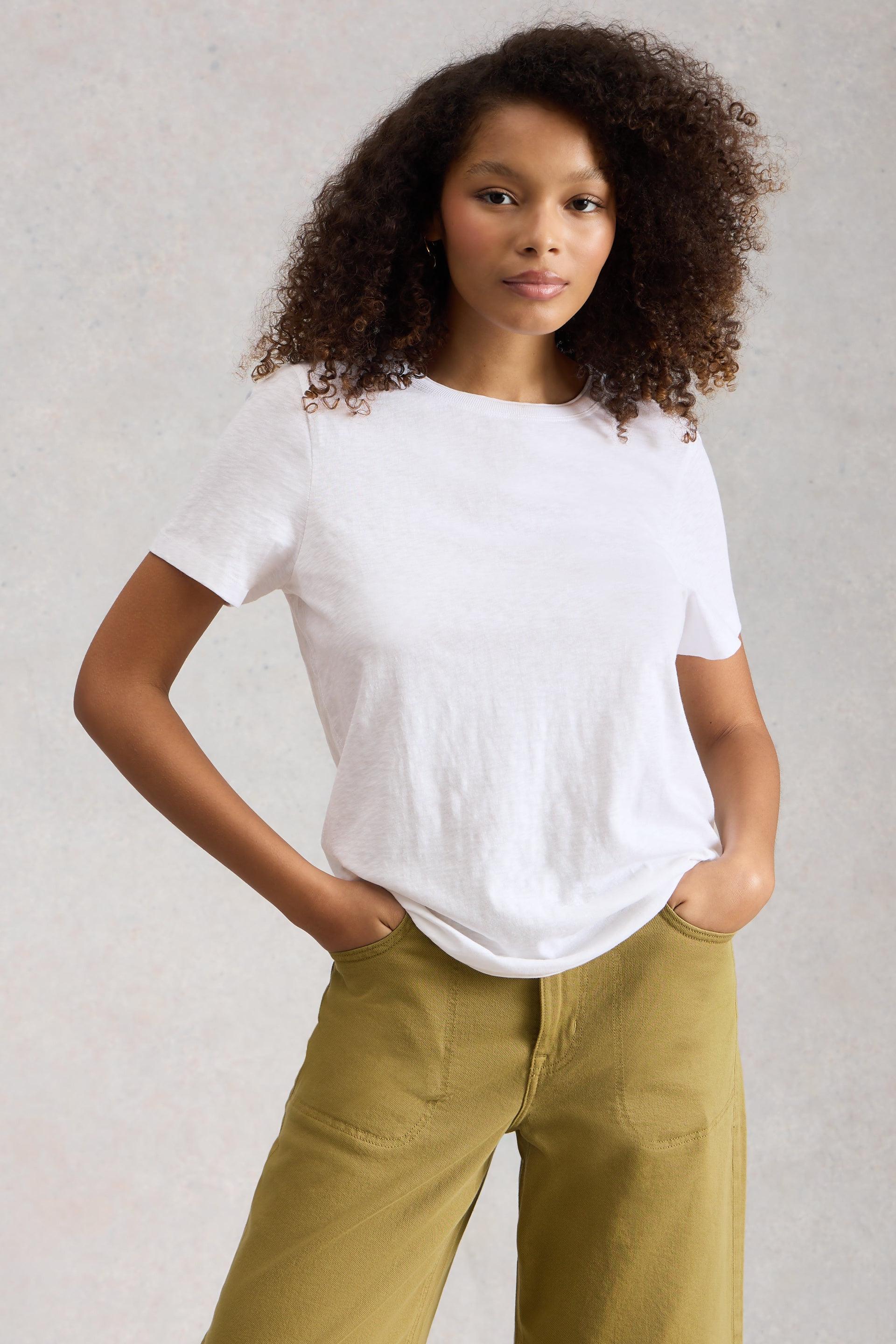 Person wearing a white cotton t-shirt and green pants against a plain background