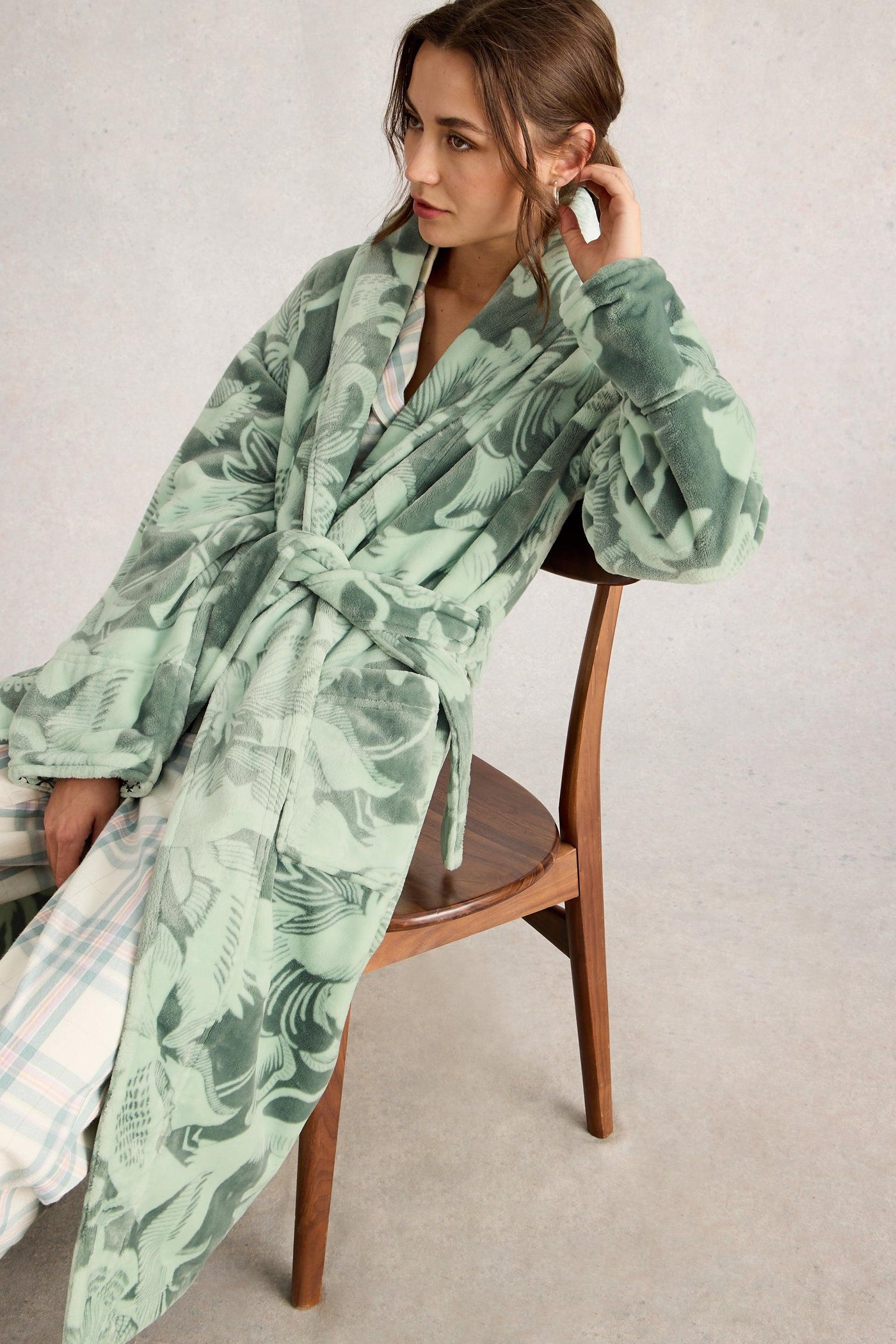Woman wearing a green patterned robe sitting on a chair against a plain background
