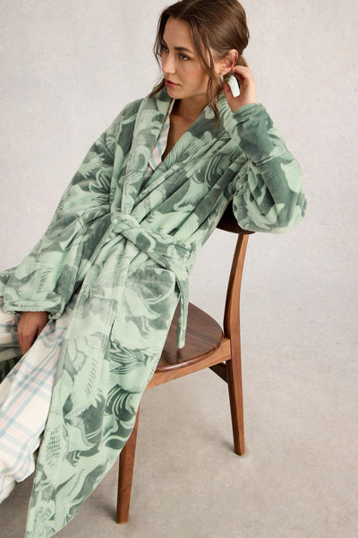 Woman wearing a green patterned robe sitting on a chair against a plain background