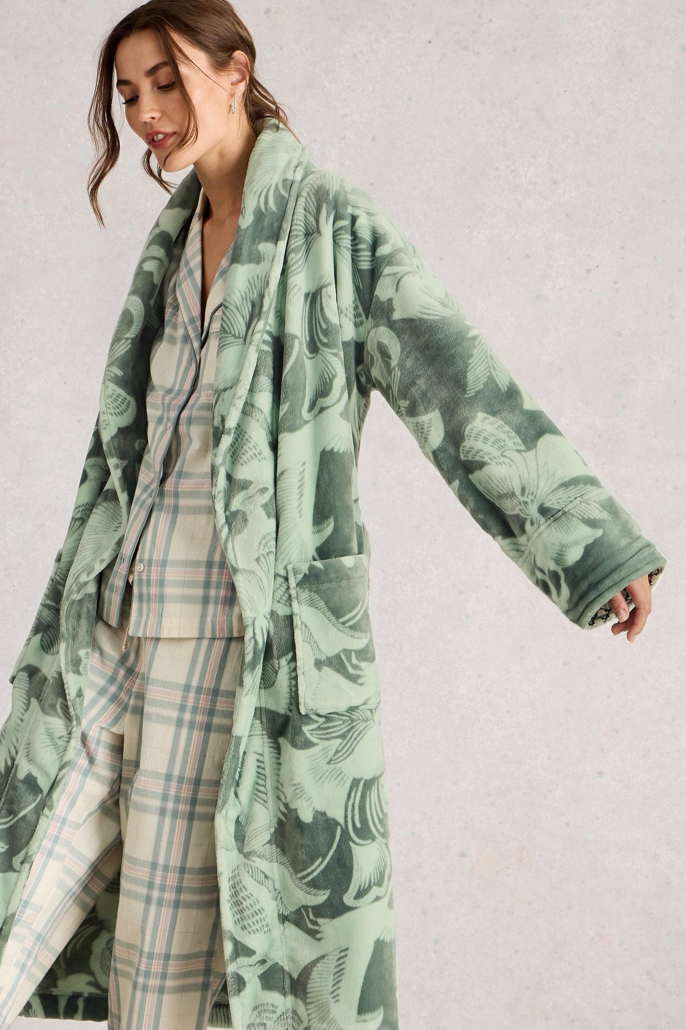 Woman wearing a green patterned dressing gown over a plaid outfit on a light gray background