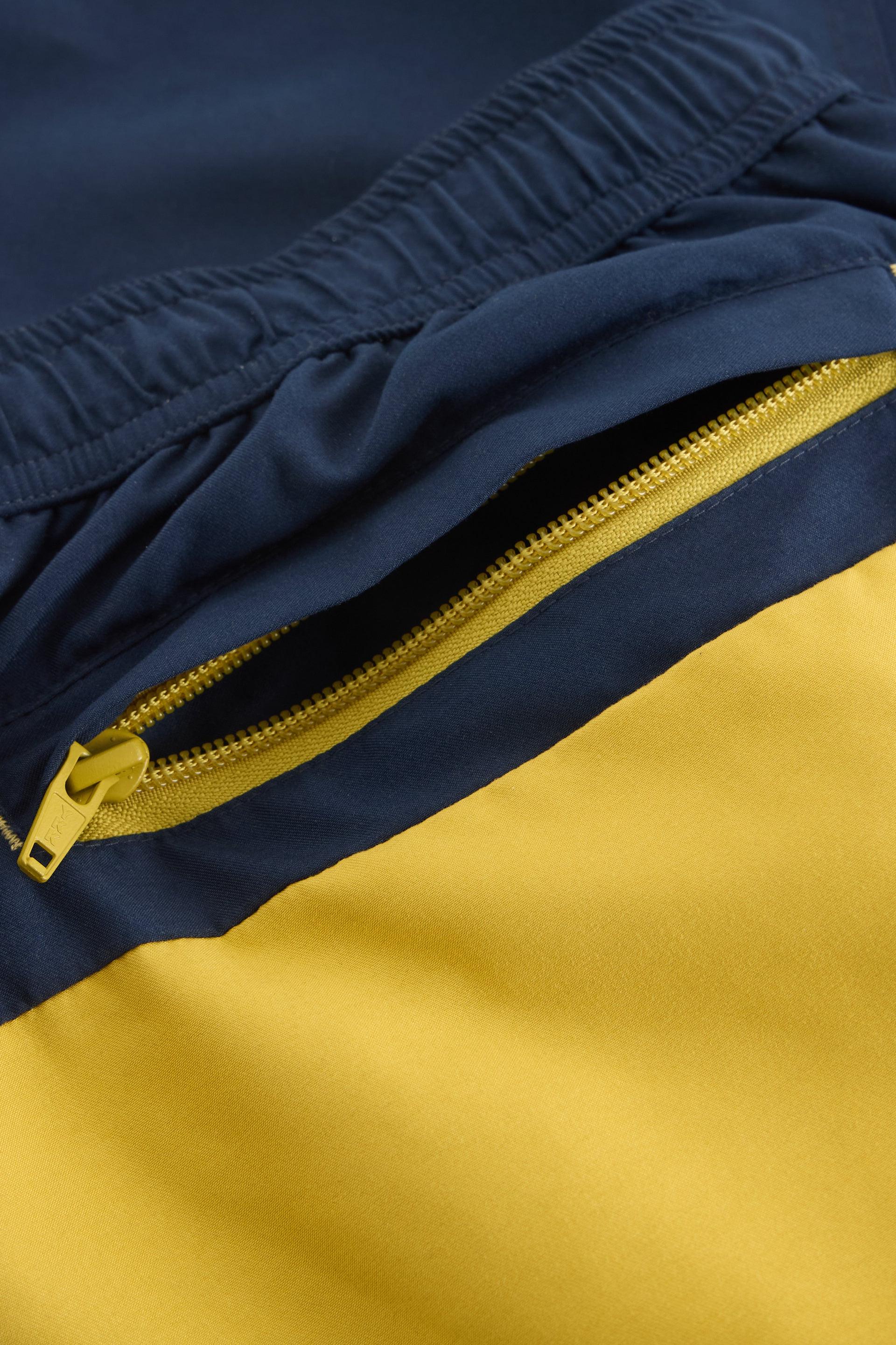 Close up of yellow zipped pocket on back of white stuff swimshorts.