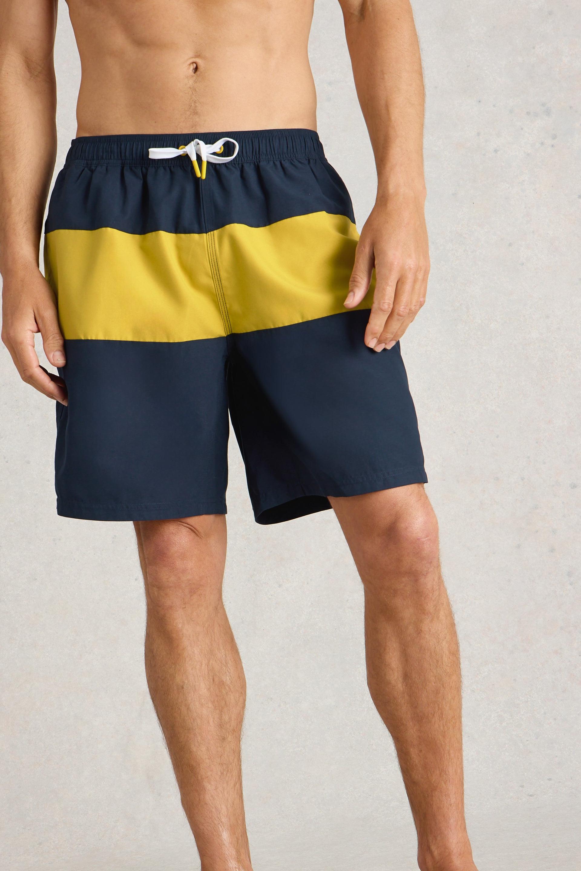 Model wearing navy and yellow colourblock beach shorts with white drawstring.