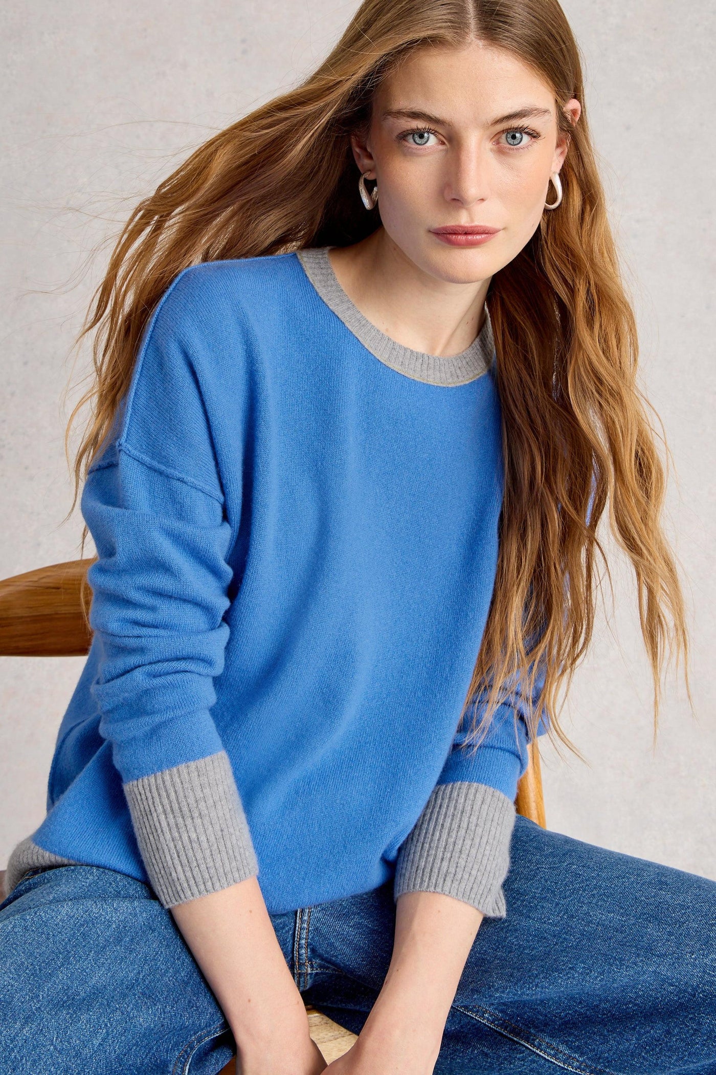 Woman wearing a blue cashmere sweater with gray trim sitting on a chair.