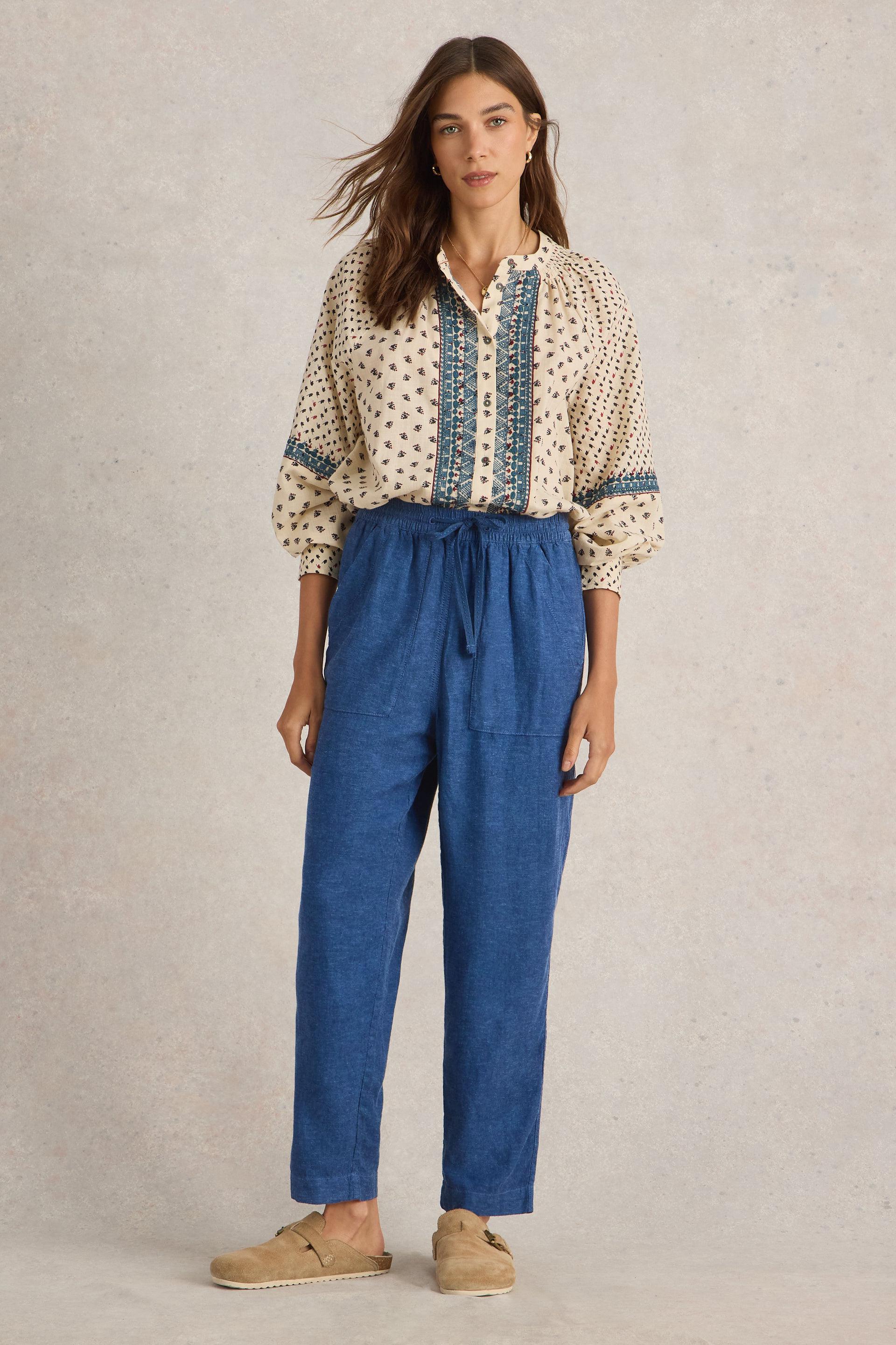 Model wearing blue linen trousers paired with printed blouse and beige clogs.