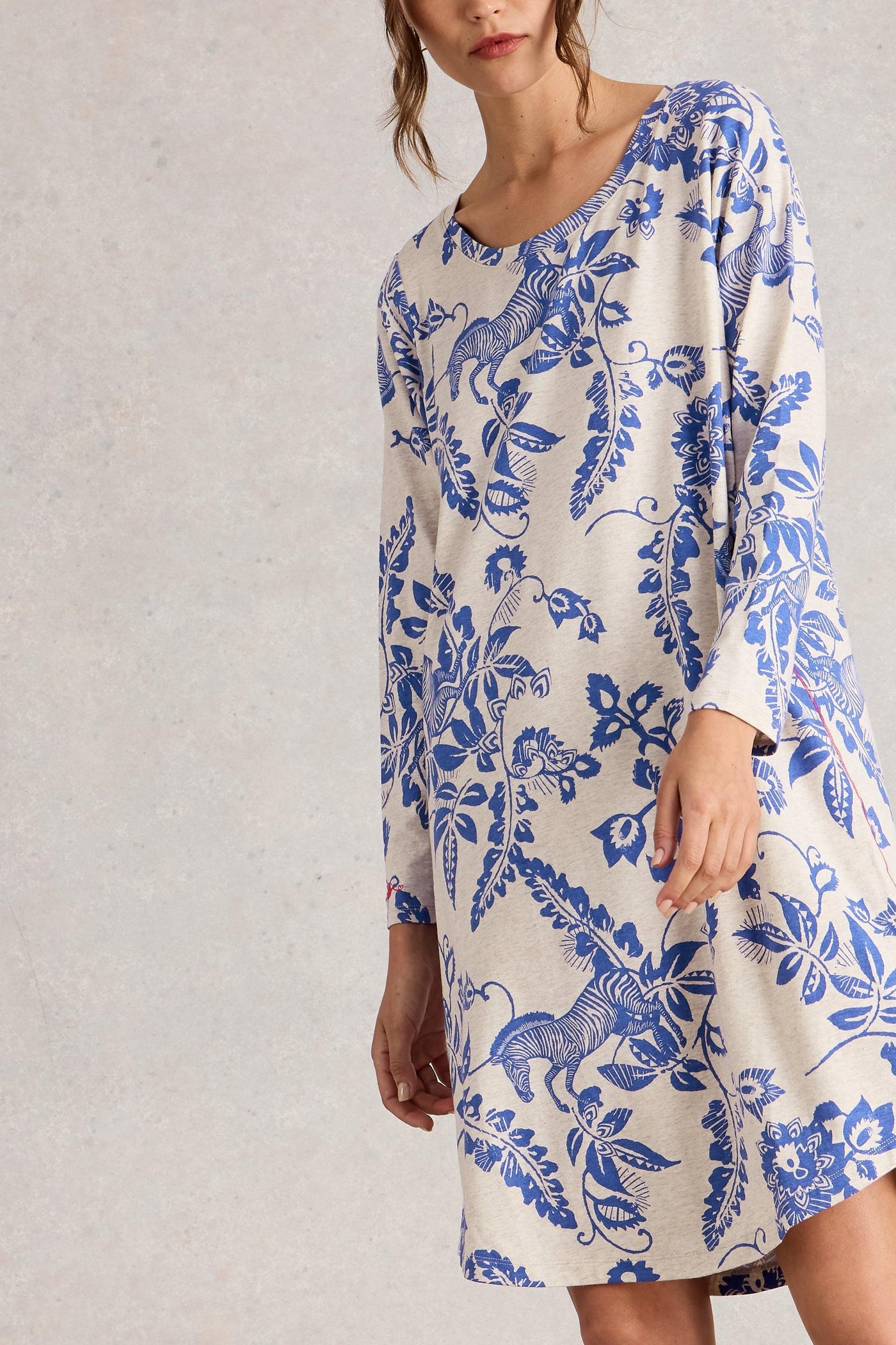 Woman wearing a long-sleeve night dress with blue floral pattern on a plain background