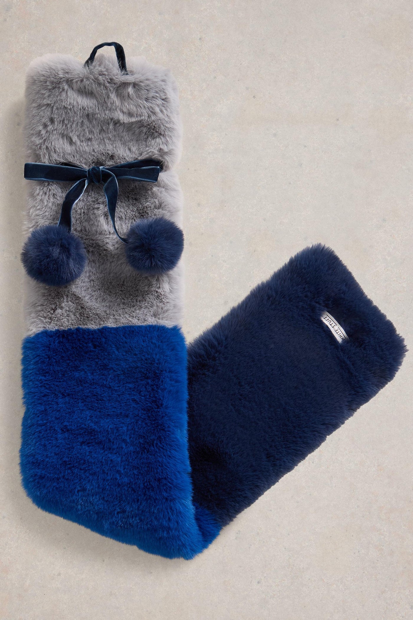 Gray and blue fuzzy hot water bottle with pom-poms on a beige background