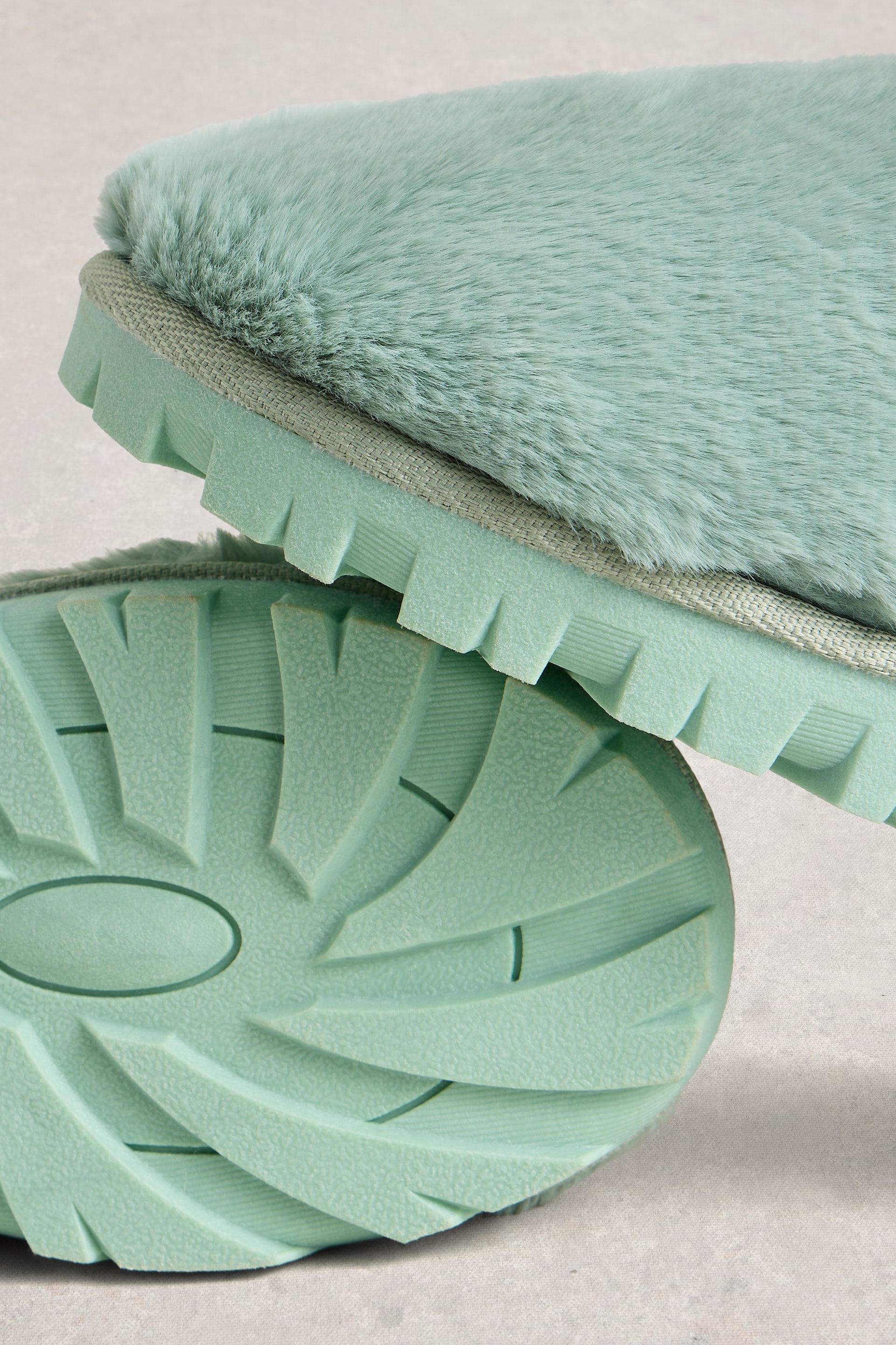 Green slippers with textured sole and plush lining on a light background