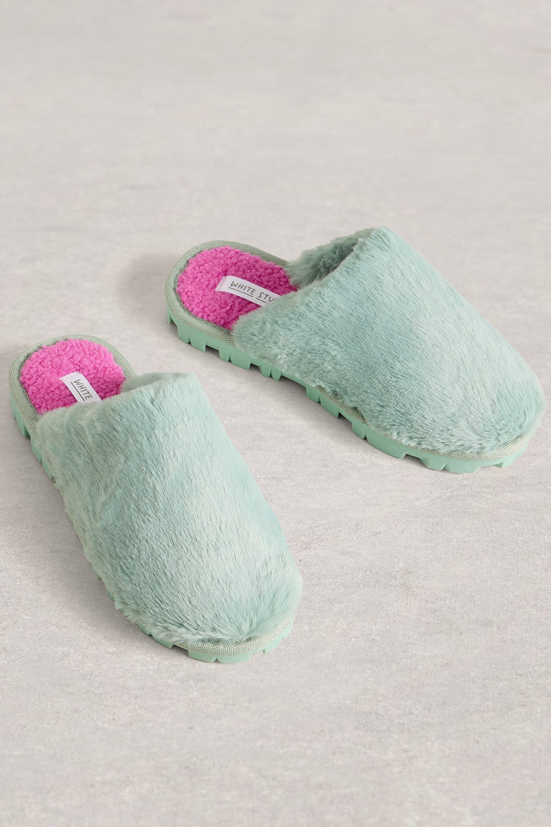 Pair of green slippers with pink interior on a light gray background