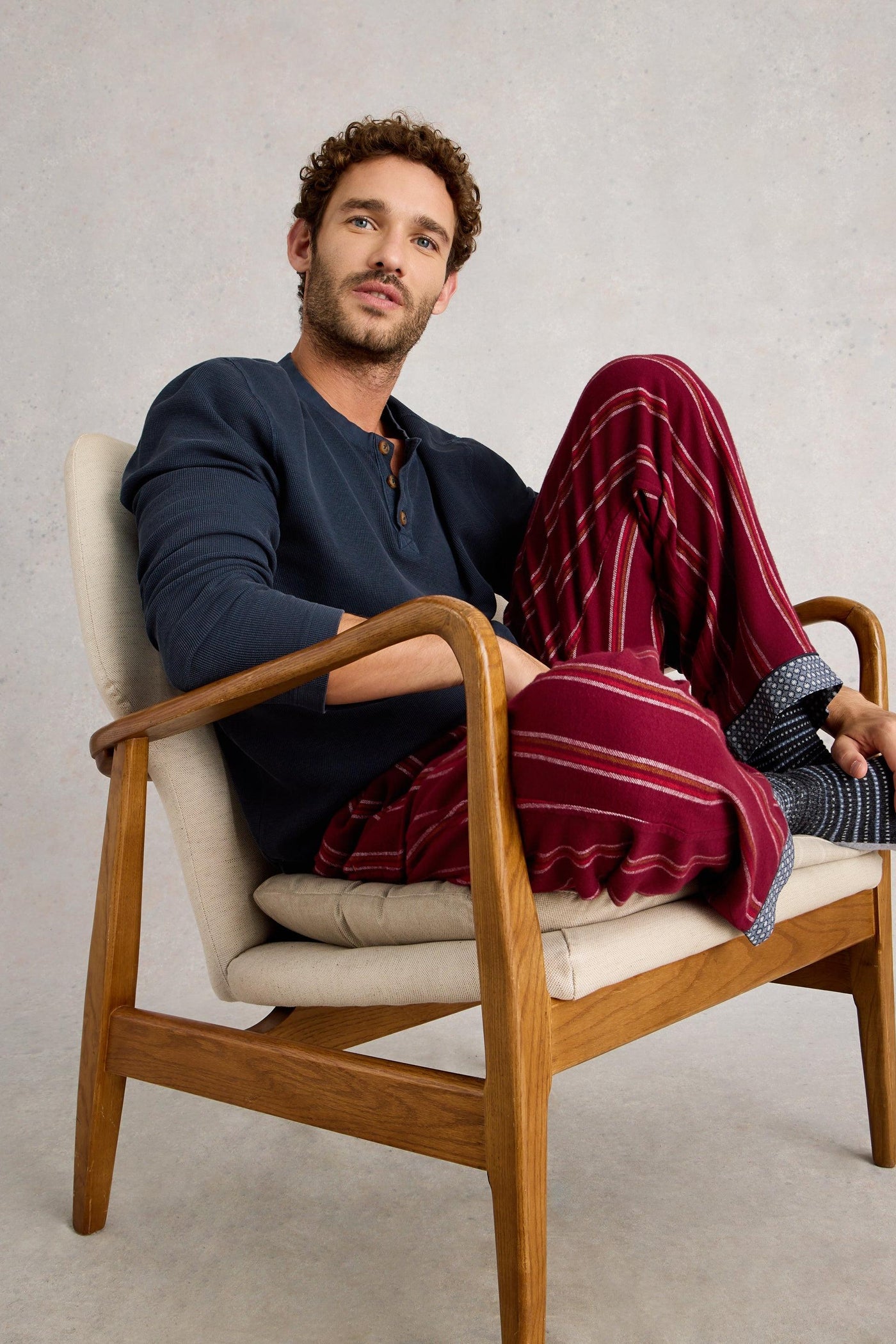 Man sitting in a chair wearing a navy organic cotton top and red plaid pants against a plain background