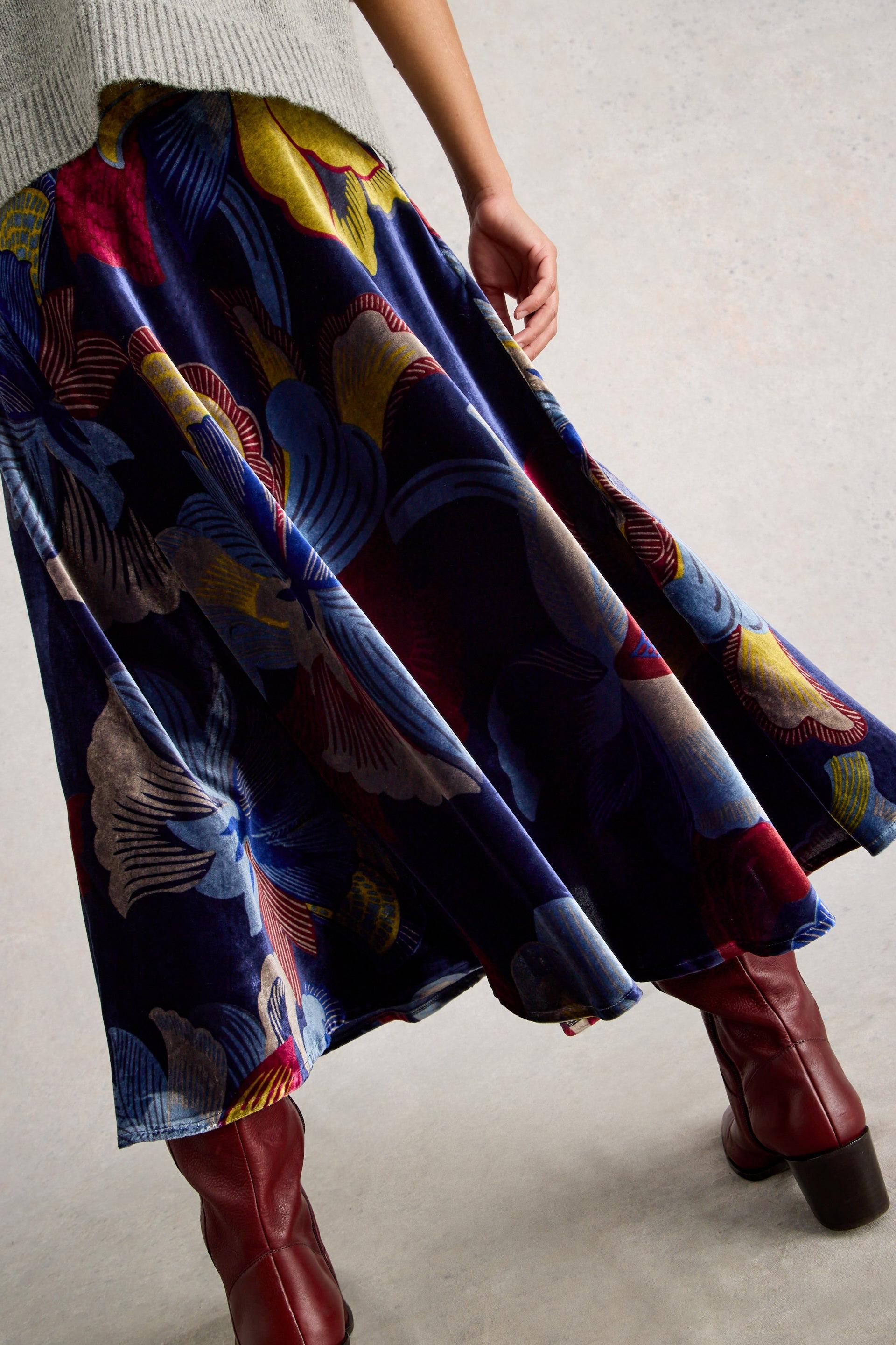 Person wearing a colorful patterned skirt and red boots on a neutral background