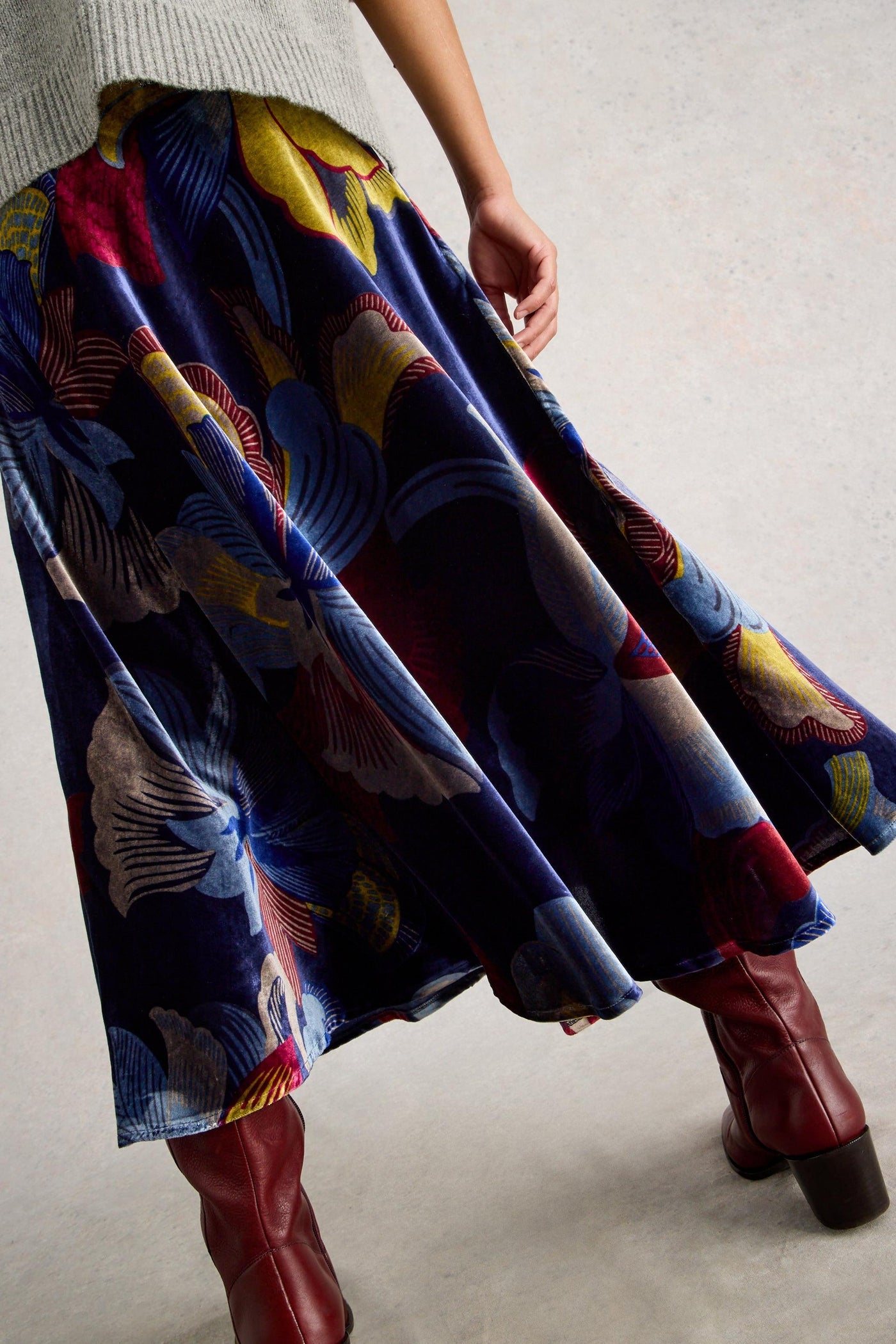 Person wearing a colorful patterned skirt and red boots on a neutral background