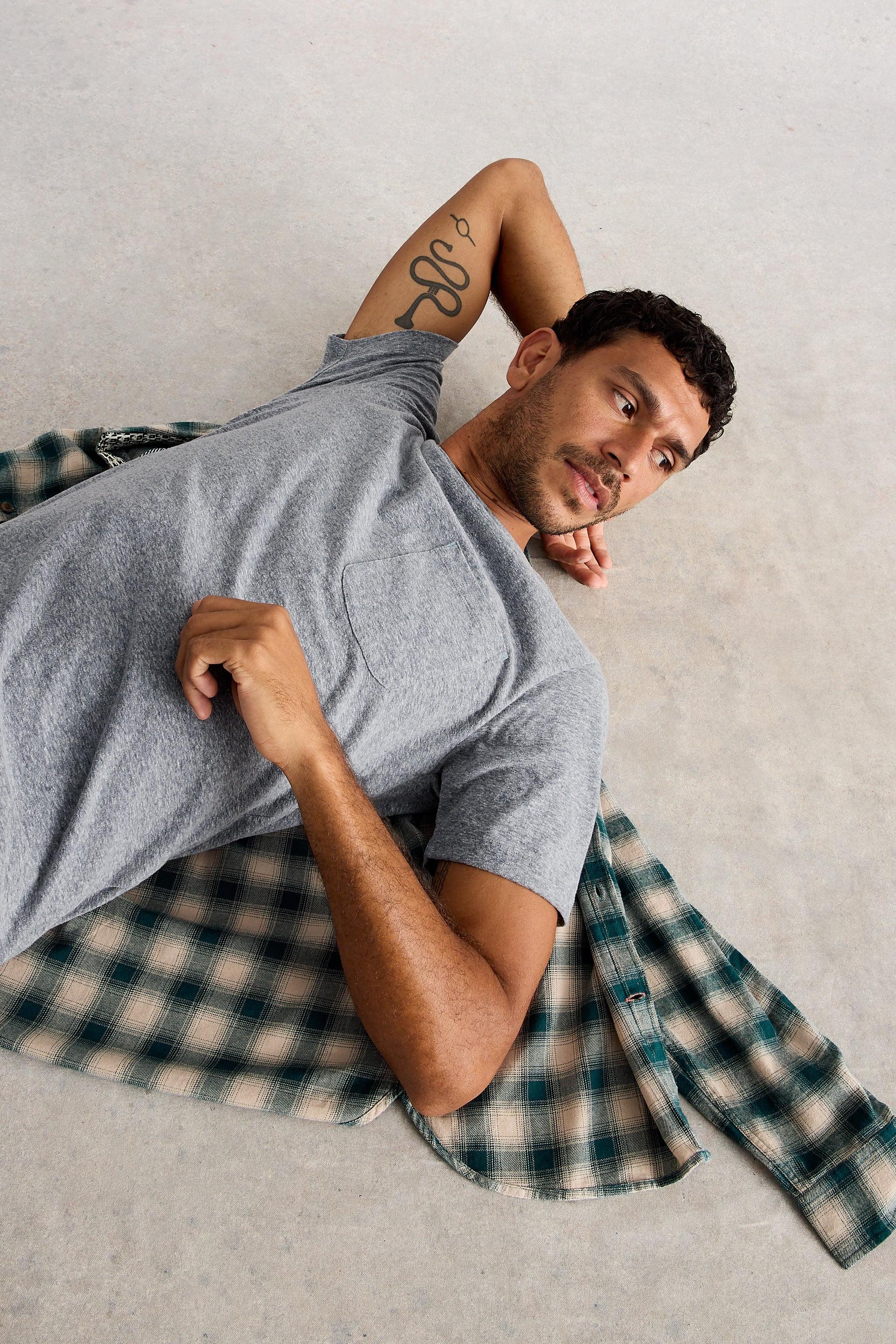 Man lying down on the floor wearing grey organic cotton short sleeved t-shirt