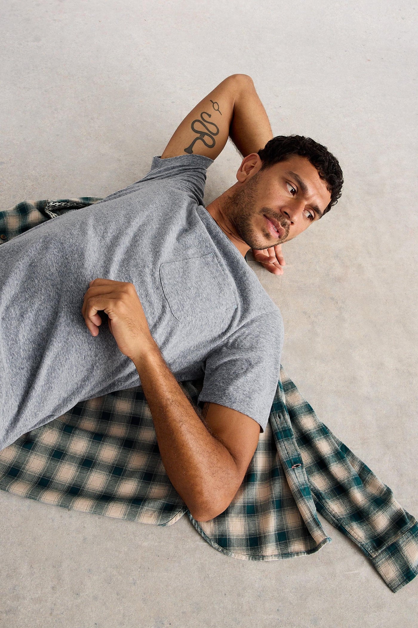 Man lying down on the floor wearing grey organic cotton short sleeved t-shirt