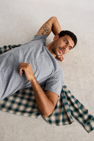 Man lying down on the floor wearing grey organic cotton short sleeved t-shirt